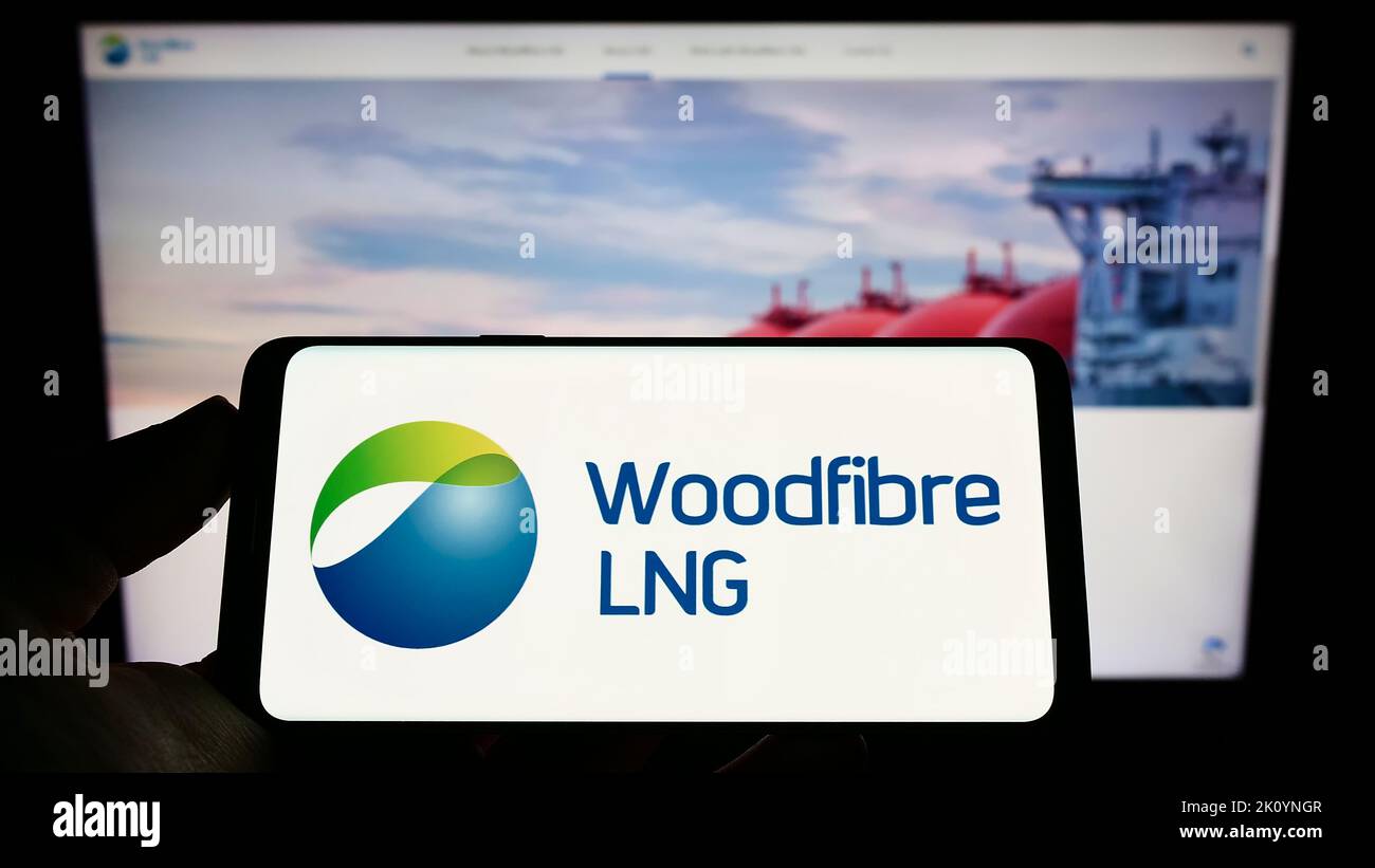 Person, die ein Mobiltelefon mit dem Logo des kanadischen Gasunternehmens Woodfiber LNG Limited auf dem Bildschirm vor der Webseite hält. Konzentrieren Sie sich auf die Telefonanzeige. Stockfoto