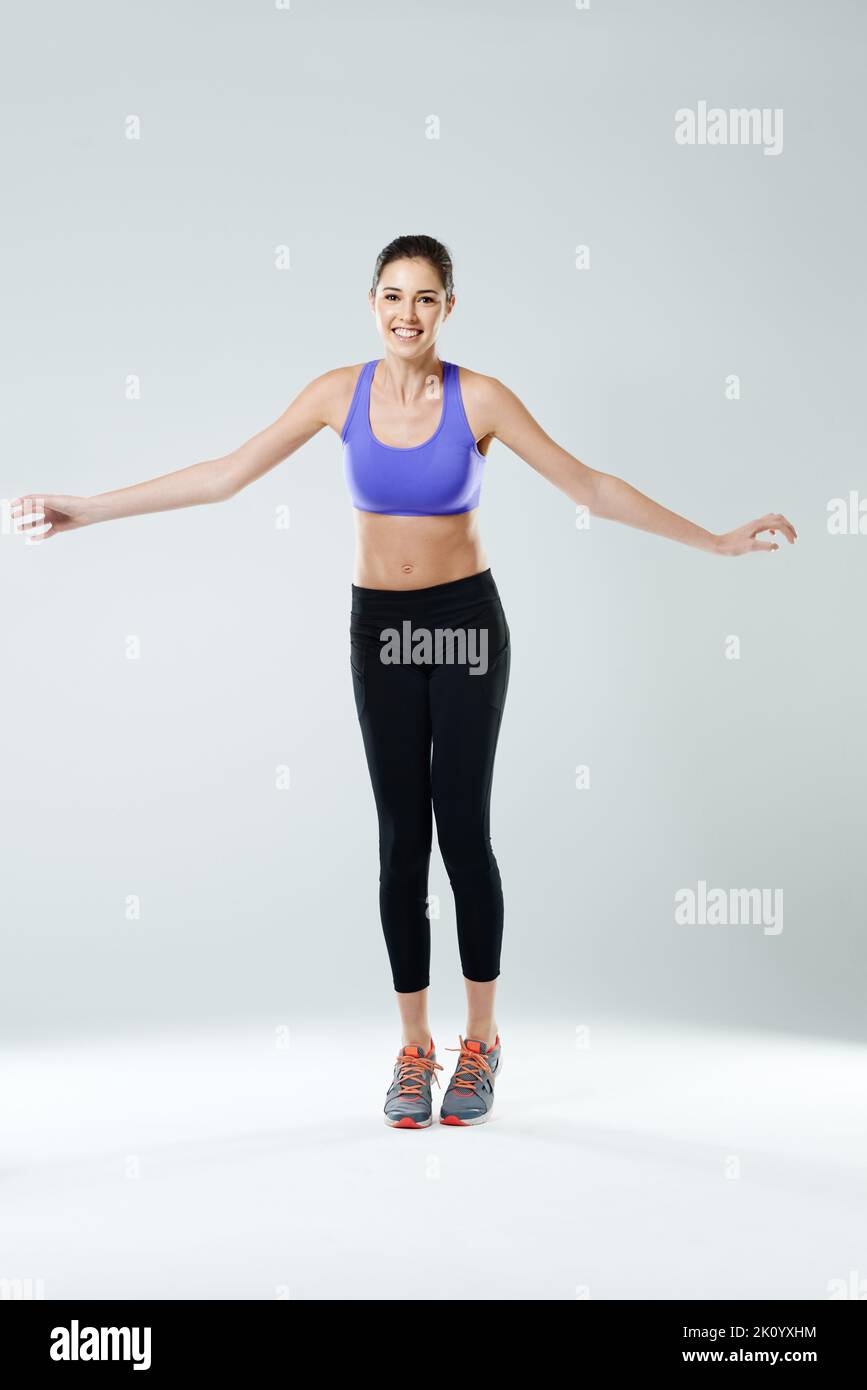 Angst ist ein Lügner. Eine glückliche junge Frau in Sportkleidung springt vor einem grauen Hintergrund. Stockfoto