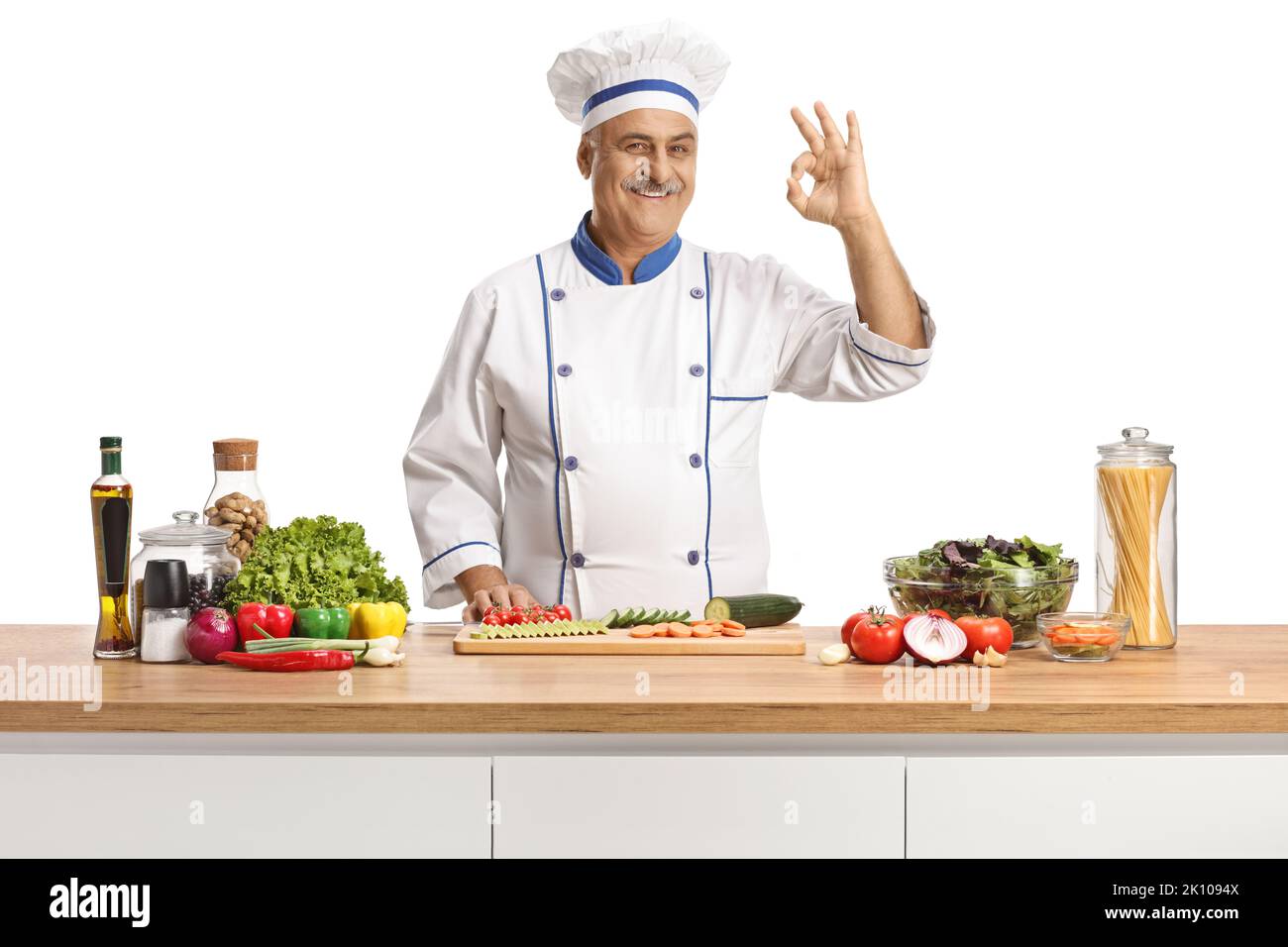 Reifer männlicher Koch posiert hinter einer Theke mit Gemüse und gestikiert gut isoliert auf weißem Hintergrund Stockfoto