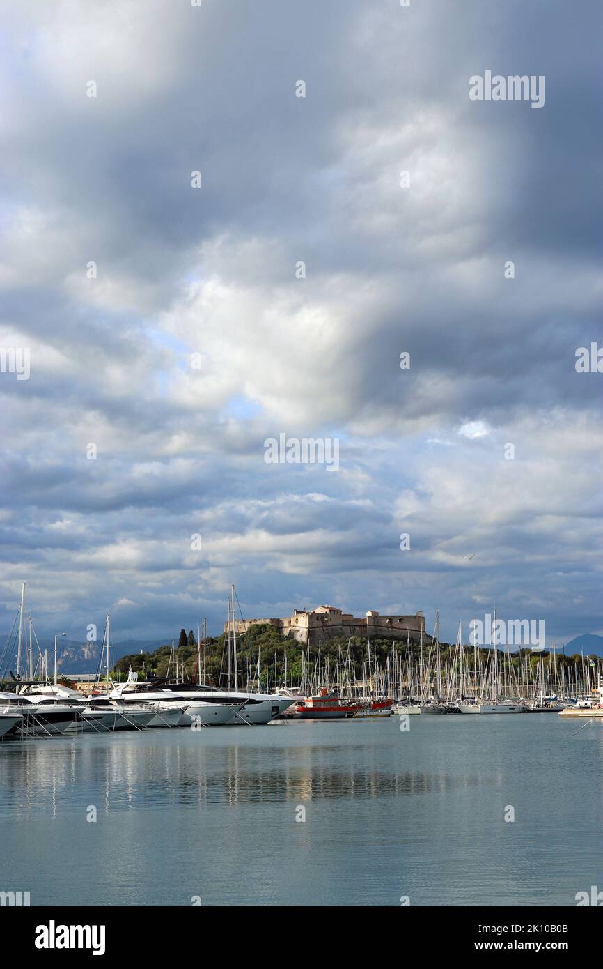 In der Ferne liegt der alte Hafen von Antibes, der „Milliardärskai“, der größte Yachthafen Europas und dahinter das historische Fort Carré, das von der Sonne in einem stürmischen Himmel beleuchtet wird Stockfoto