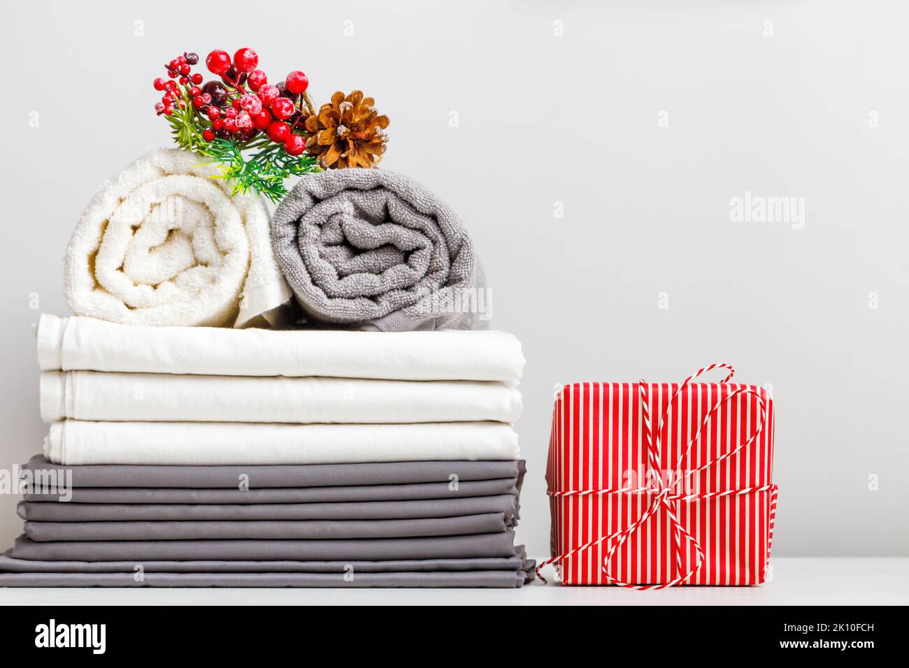 Gefaltete Handtücherrollen und Bettwäsche, Bettwäsche auf dem Tisch mit weihnachtlicher Dekoration und einem Geschenk. Stockfoto