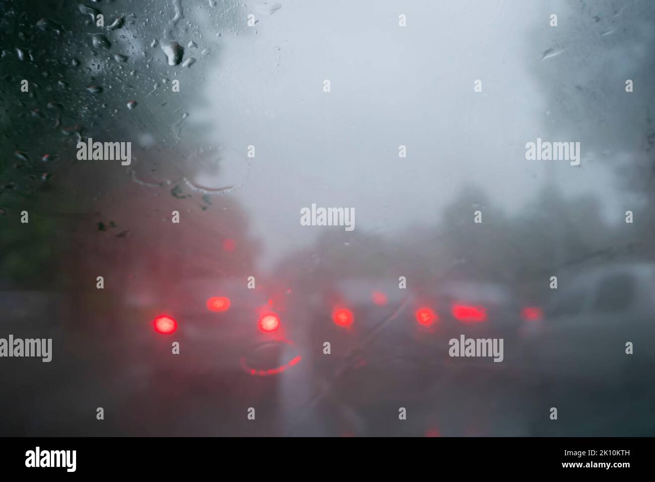 Rote Hintergrundbeleuchtung von Autos. Bild aufgenommen durch Regentropfen, die auf nasses Glas fallen, abstrakte Verkehrsunschärfen - Monsun-Stockbild von Kalkutta (ehemals Kalkutt Stockfoto