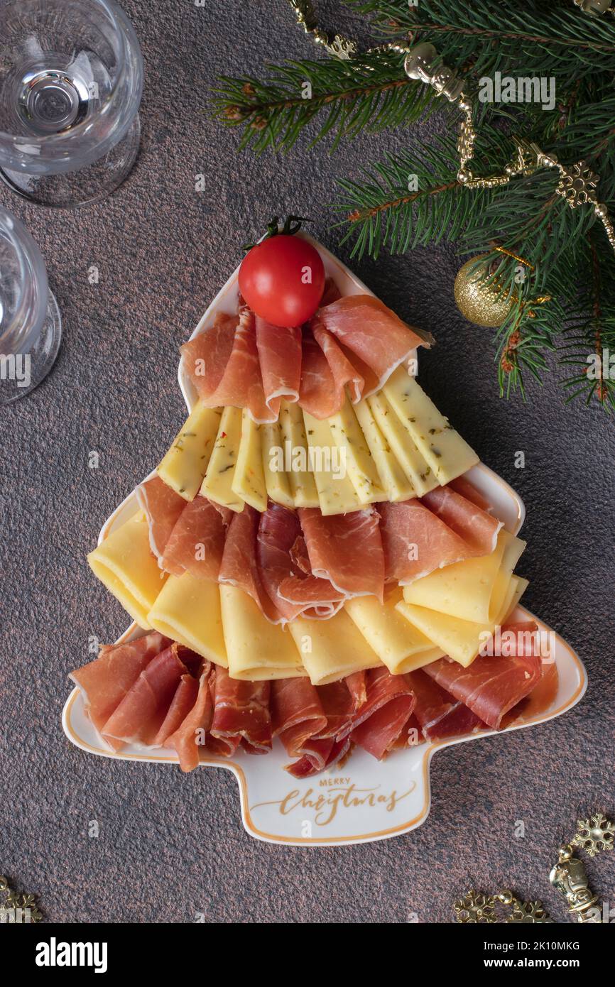 Vorspeise mit Schinken und Käse in baumförmiger weihnachtlicher Platte und Gläsern auf braunem Tisch Stockfoto