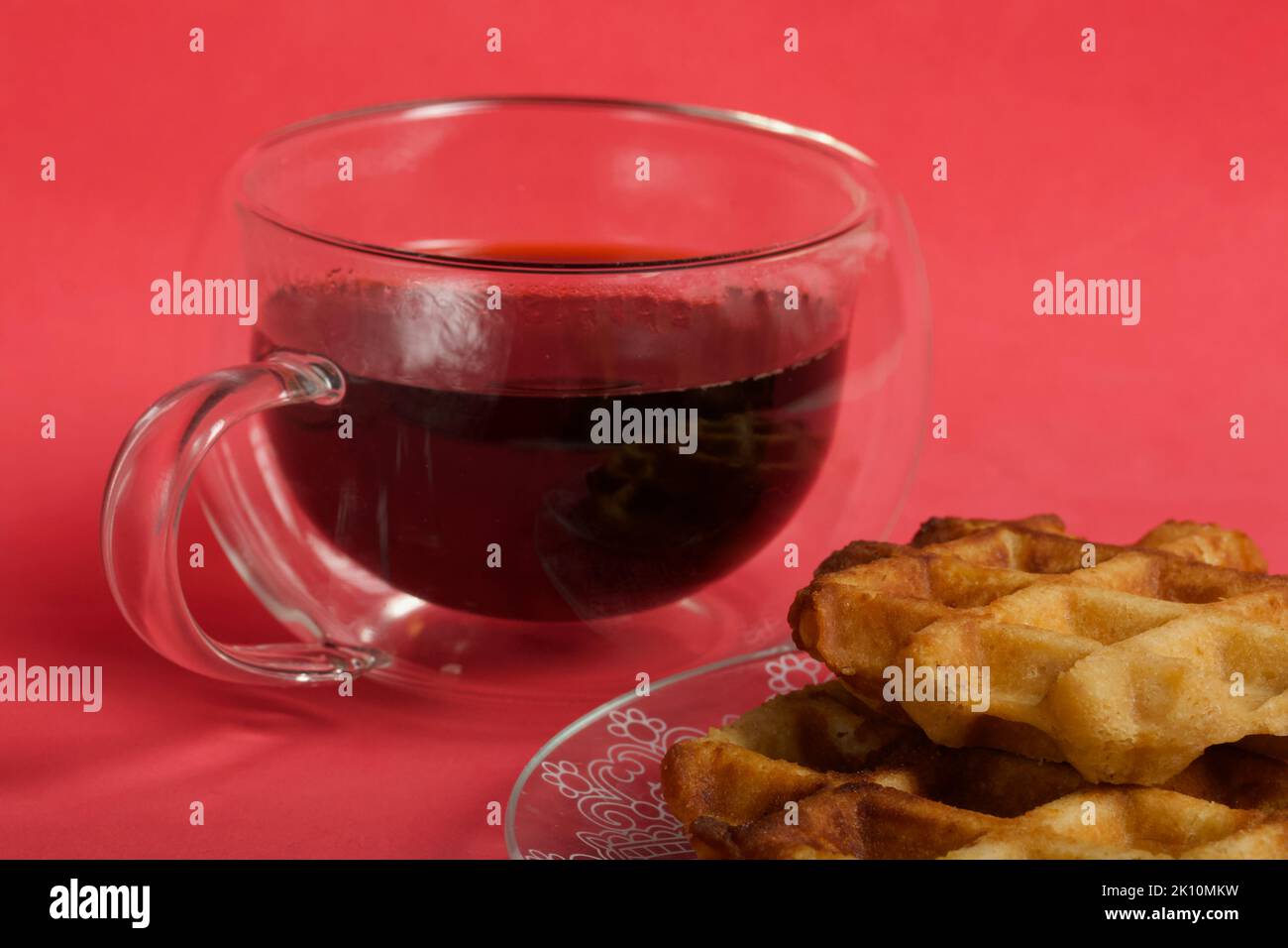Flauschige Waffeln. Sie liegen auf einer Untertasse. Neben einer Tasse Kaffee. Der Hintergrund ist rosa. Nahaufnahme. Stockfoto