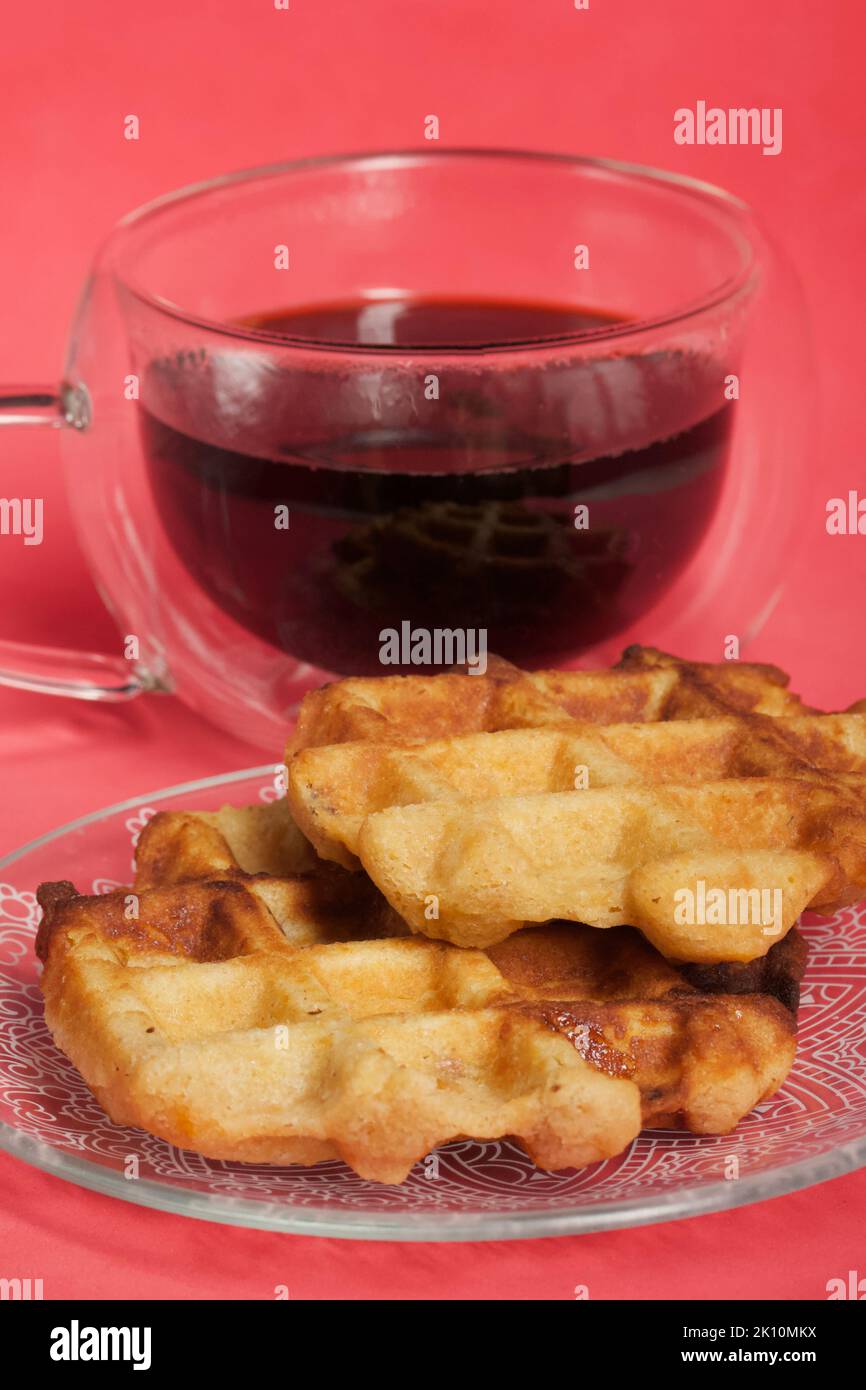 Flauschige Waffeln. Sie liegen auf einer Untertasse. Neben einer Tasse Kaffee. Der Hintergrund ist rosa. Nahaufnahme. Stockfoto