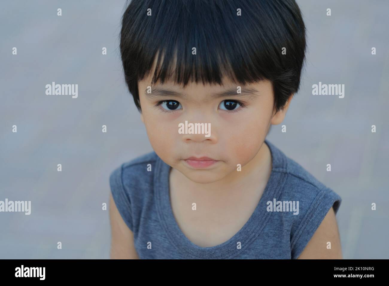 Netter philippinischer Junge, etwa 5 Jahre alt, schaut vor die Kamera. Nahaufnahme eines Tages im Freien mit einem jungen asiatischen Kind mit glänzendem, glattem Haar und schwarzen Augen. Stockfoto