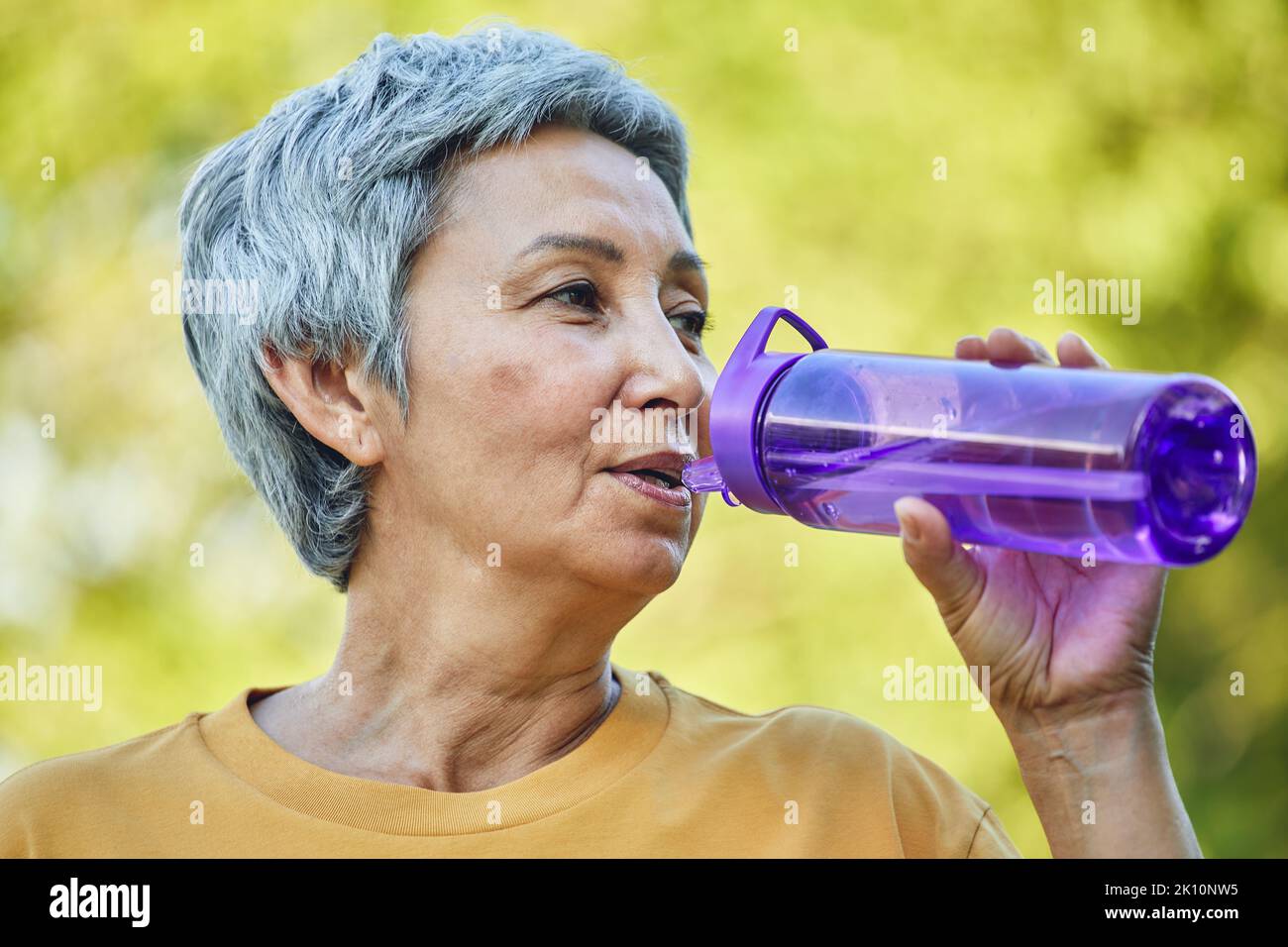 Close up image Attraktive reife Frau hält Kunststoff wiederverwendbare Flasche machen Schluck trinken noch Mineralwasser während des Morgens trainieren oder spazieren im Sommer Stockfoto