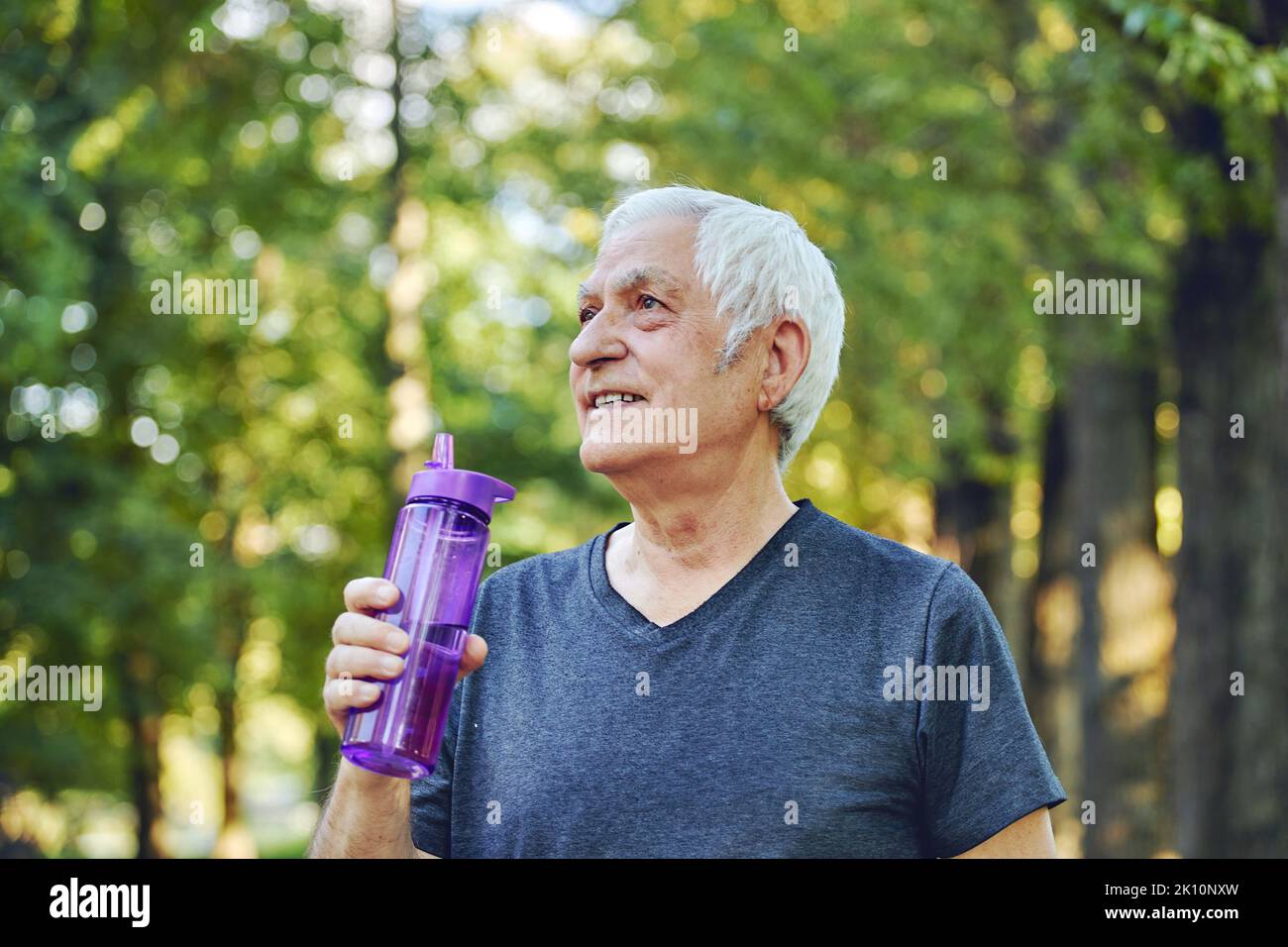 Close up image attraktiver reifer Mann hält wiederverwendbare Plastikflasche trinkt stilles Mineralwasser während des Morgens trainieren oder spazieren im Sommerpark, Cari Stockfoto