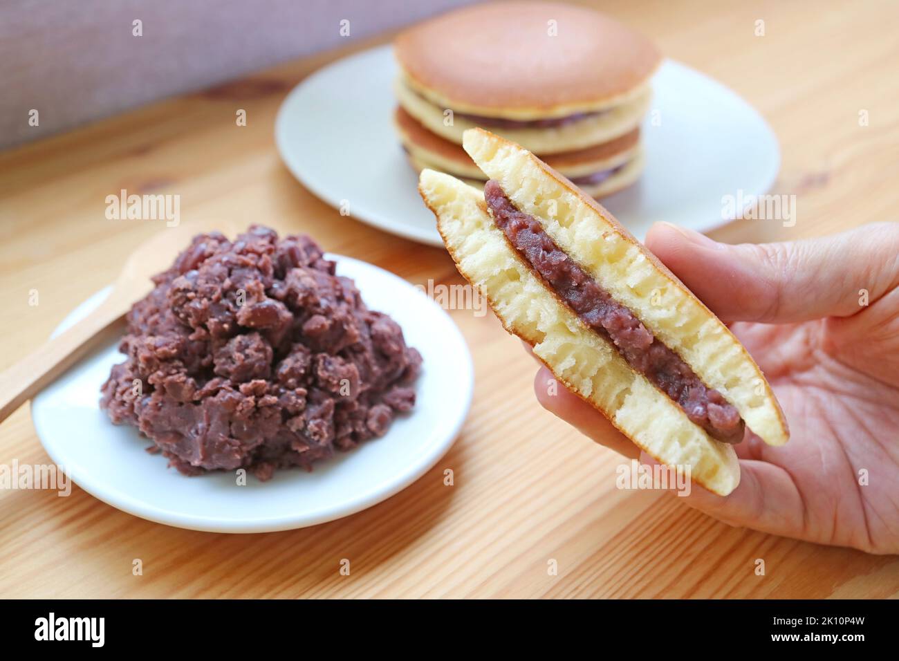 Ein Stück halb Dorayaki in der Hand mit einer Platte aus roter Bean Paste auf Holztisch Stockfoto