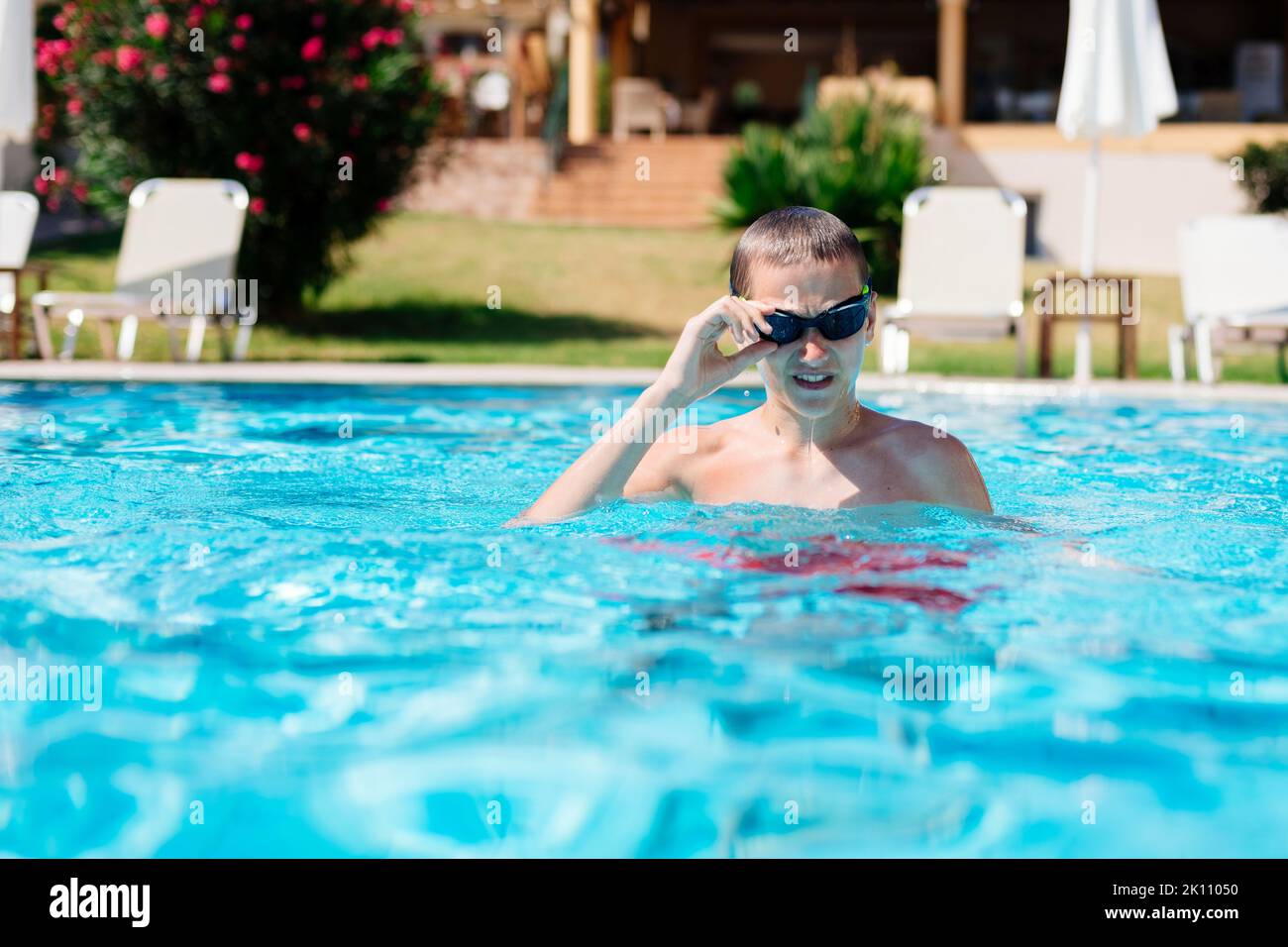 Ein sportlicher Teenager passt seine Schwimmbrille an, während er in einem Schwimmbad steht Stockfoto