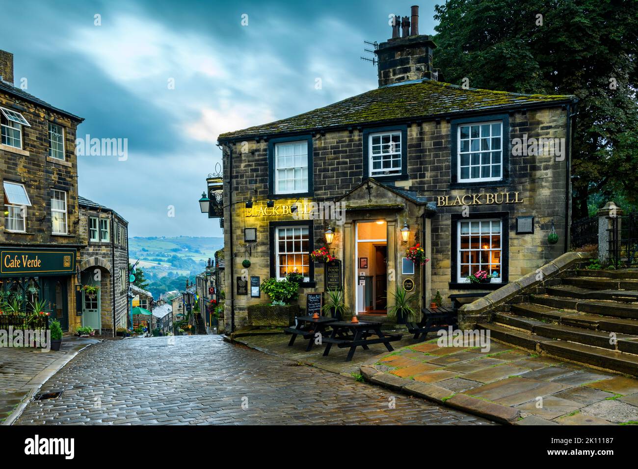 Haworth Main Street (steiler Hügel, alte Gebäude, blaues Abendlicht, historisches Bronte-Schwesterndorf, Pub der Klasse 2) - West Yorkshire, England, Großbritannien. Stockfoto