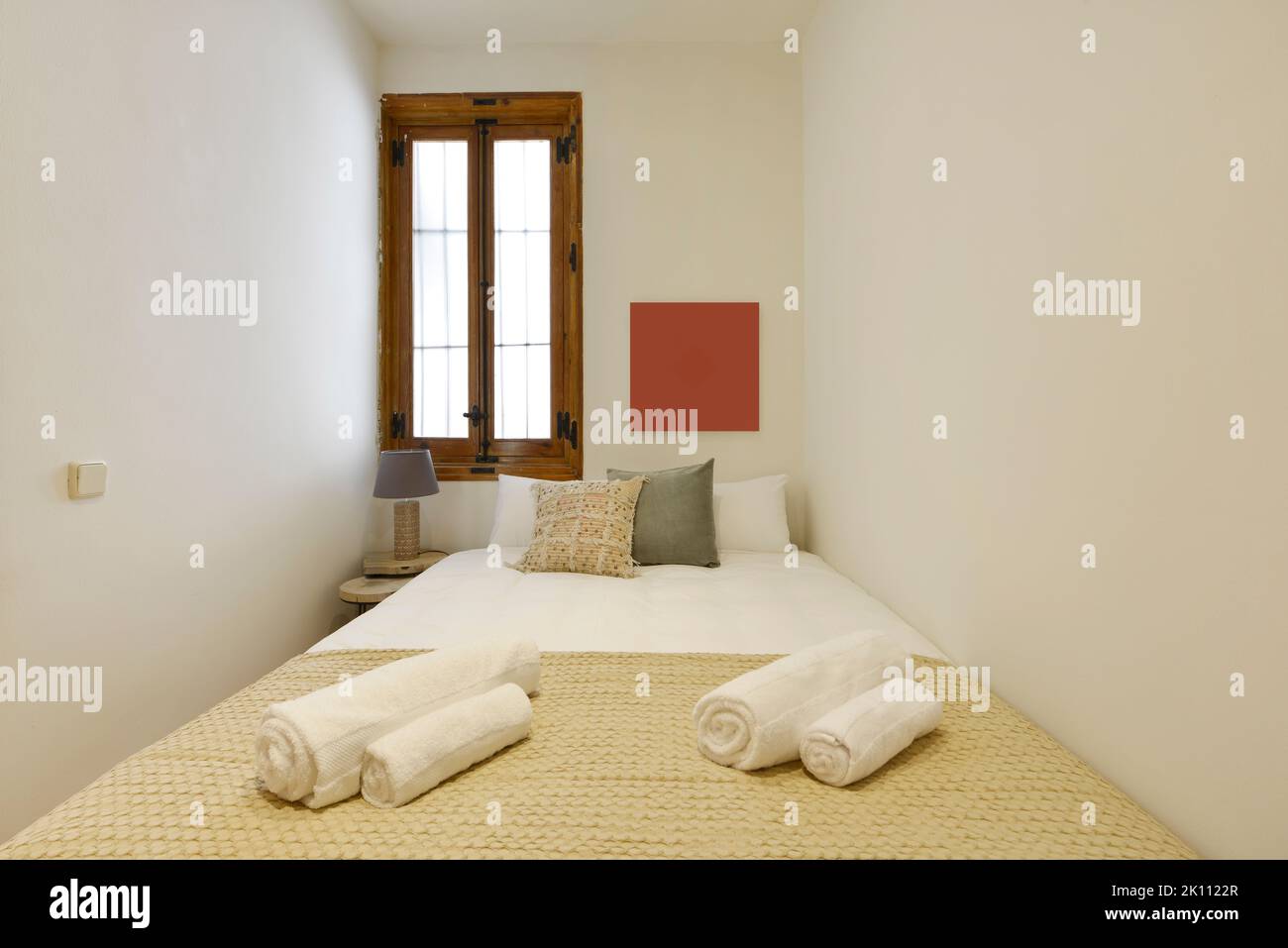 Kleines Schlafzimmer mit Doppelbett, passenden Kissen, passendem Bettüberwurf und Holzfenster Stockfoto