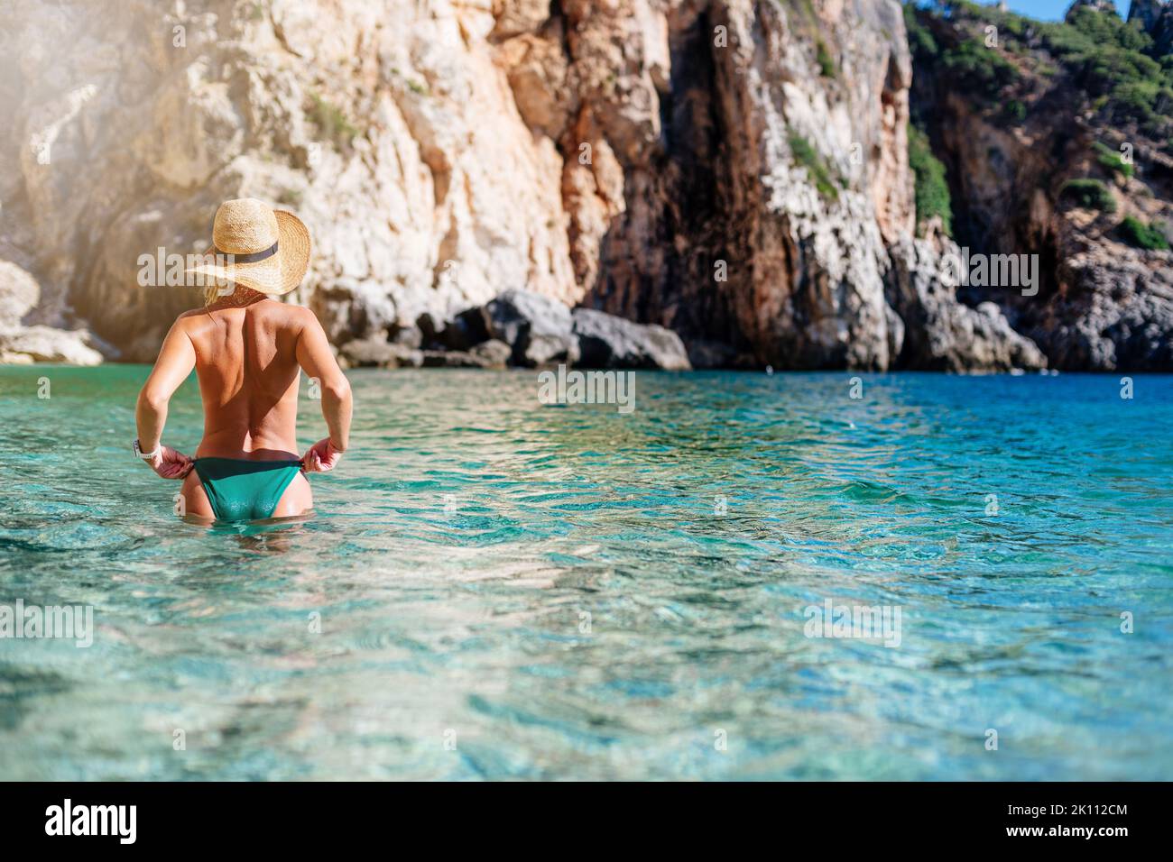 Schöne blonde Frau in einem Strohhut, die zurück im Meer an einem Strand in Korfu steht Stockfoto