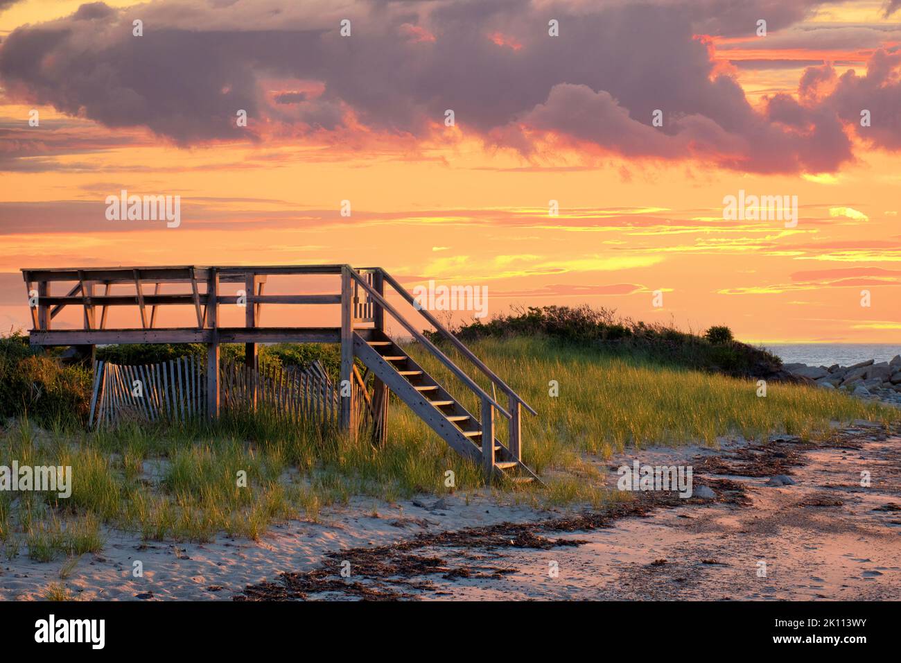 Schöne Strandszene am Cape Cod mit bunten, sonnenbeschienenen Wolken und der Sonne, die unter den Horizont fällt. Lebhafter Sonnenuntergang im Sommer, aufgenommen in Dennis. Stockfoto