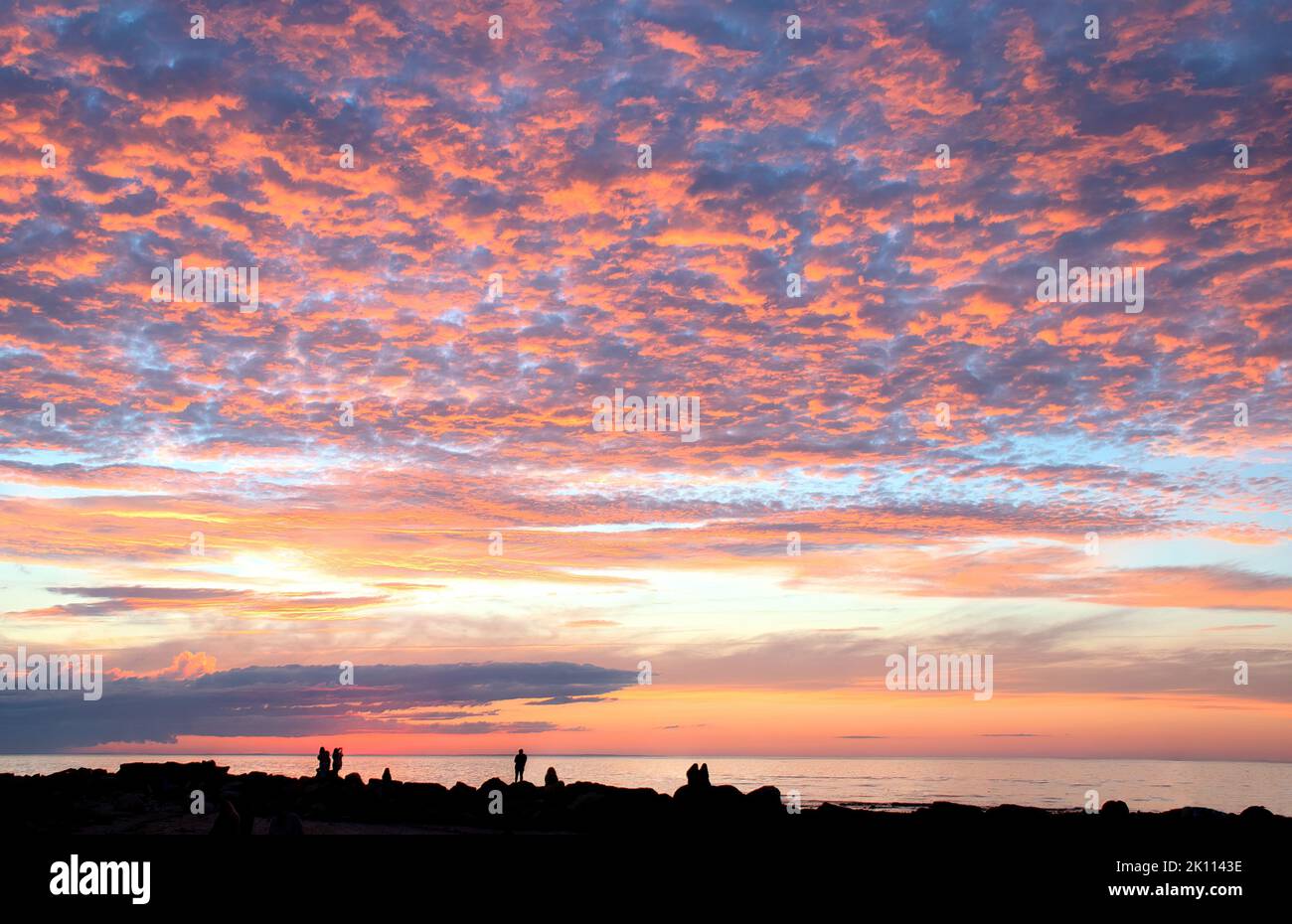 Wunderschöner Sonnenuntergang in Neuengland. Dunkle Umrisse (Silhouetten) von nicht erkennbaren Menschen entlang der Wellenfelsen am Cape Cod Beach in Dennis, Massachusetts. Stockfoto