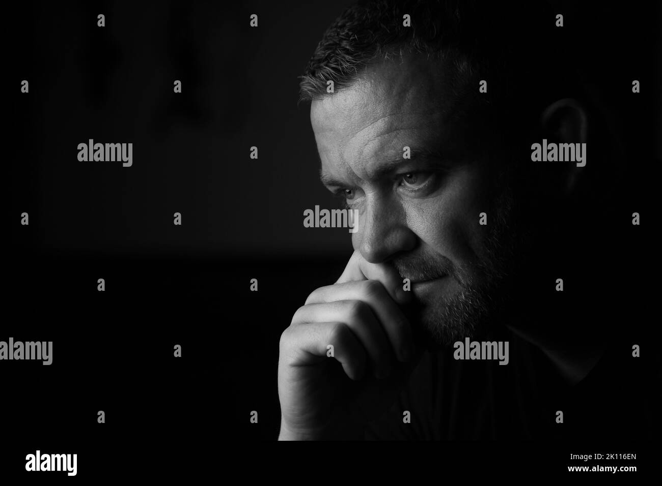 Männlich sitzt mit Hand an Mund in einem denkenden Ausdruck. Stockfoto