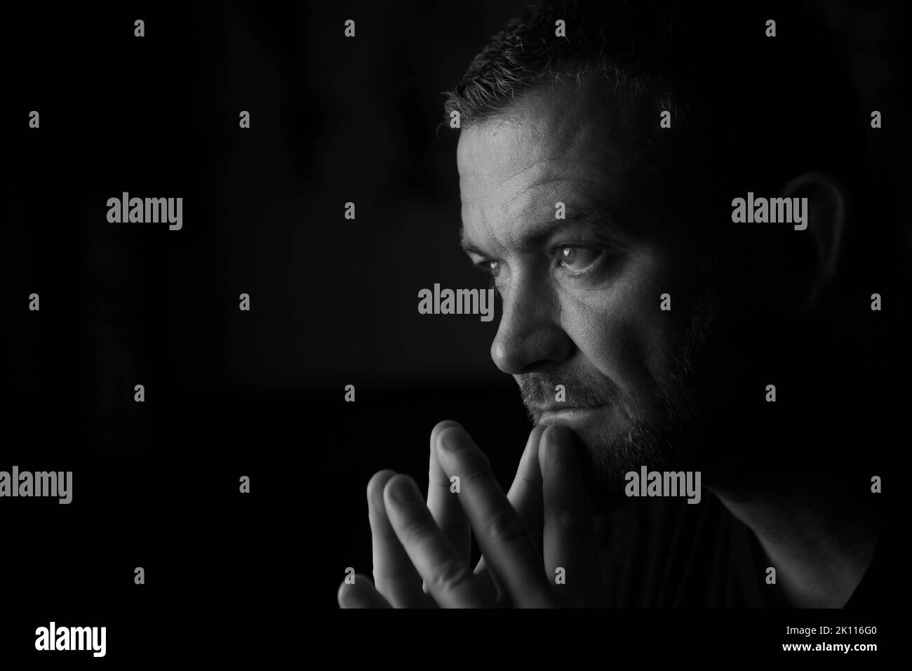 Männlich sitzt und hat Hände in der Nähe des Gesichts mit einem denkenden Ausdruck. Stockfoto