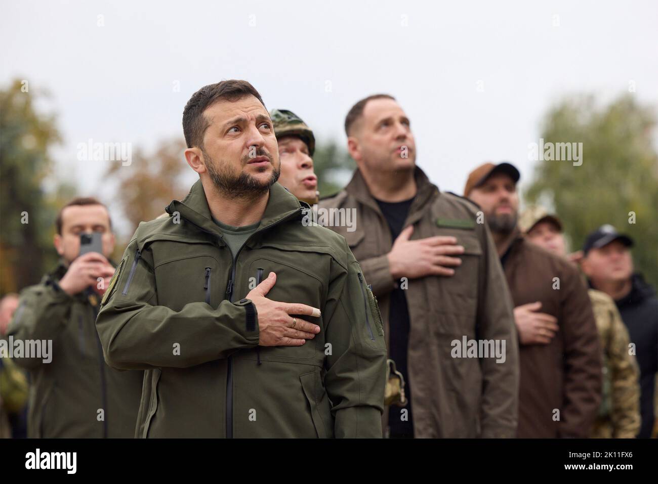 Izium, Ukraine. 14. September 2022. Der ukrainische Präsident Wolodymyr Zelenskyy, links, begrüßt, als die ukrainische Flagge über der zurückerobert Stadt während einer Zeremonie vor dem beschädigten Rathaus am 14. September 2022 in Izium, Region Charkiw, Ukraine, angehoben wird. Zelenski machte einen überraschenden Besuch in der Stadt, die während einer ukrainischen Gegenoffensive aus Russland zurück erobert wurde. Kredit: Ukrainisches Presidential Press Office/Ukraine Presidency/Alamy Live News Stockfoto