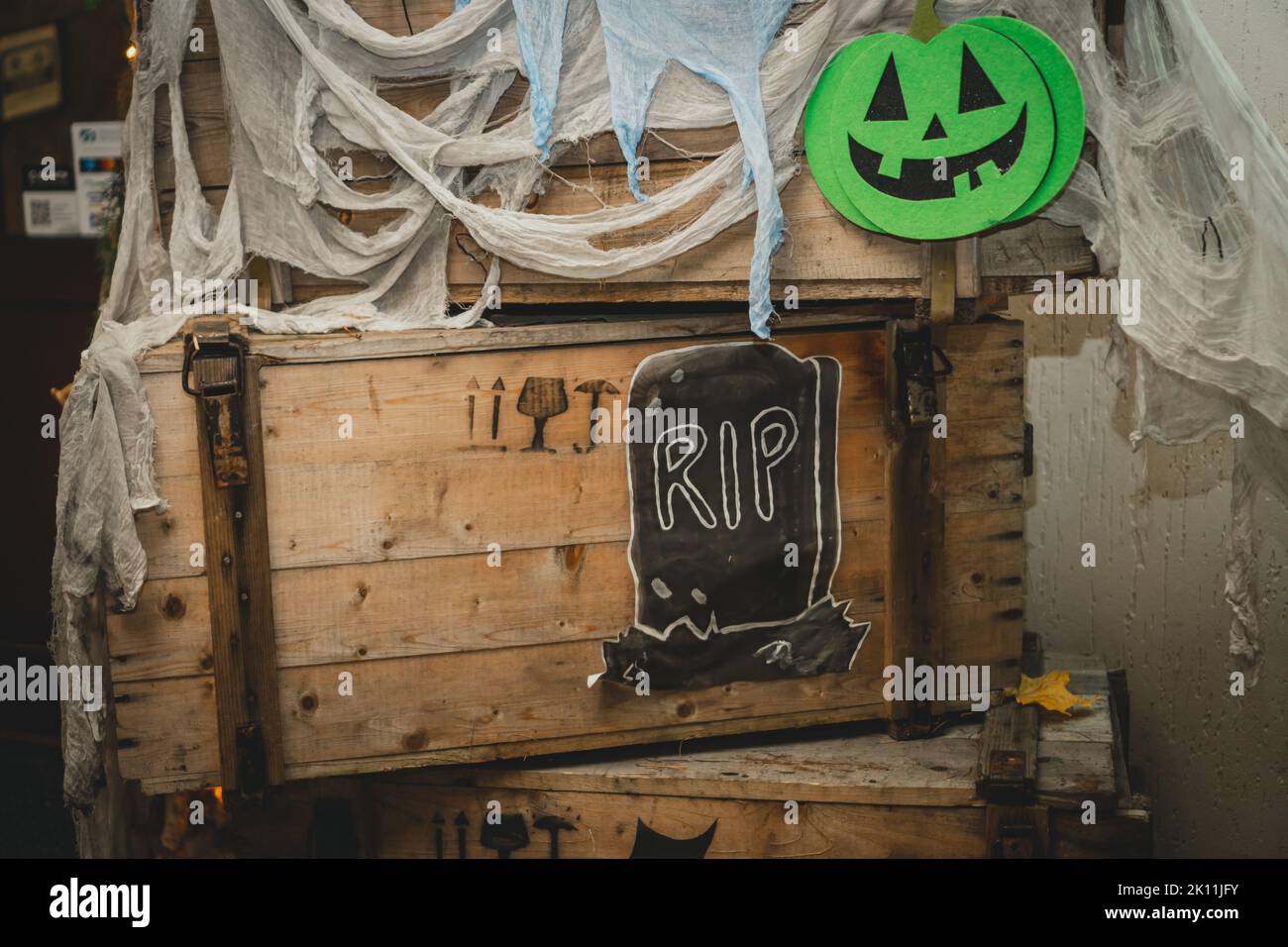Grüner, heller halloween Kürbis mit bemalter Nase, Mund und Augen auf Holzkiste mit Gaze als Netz und Grabstein mit RIP-Aufschrift. Handgefertigte Bilder Stockfoto