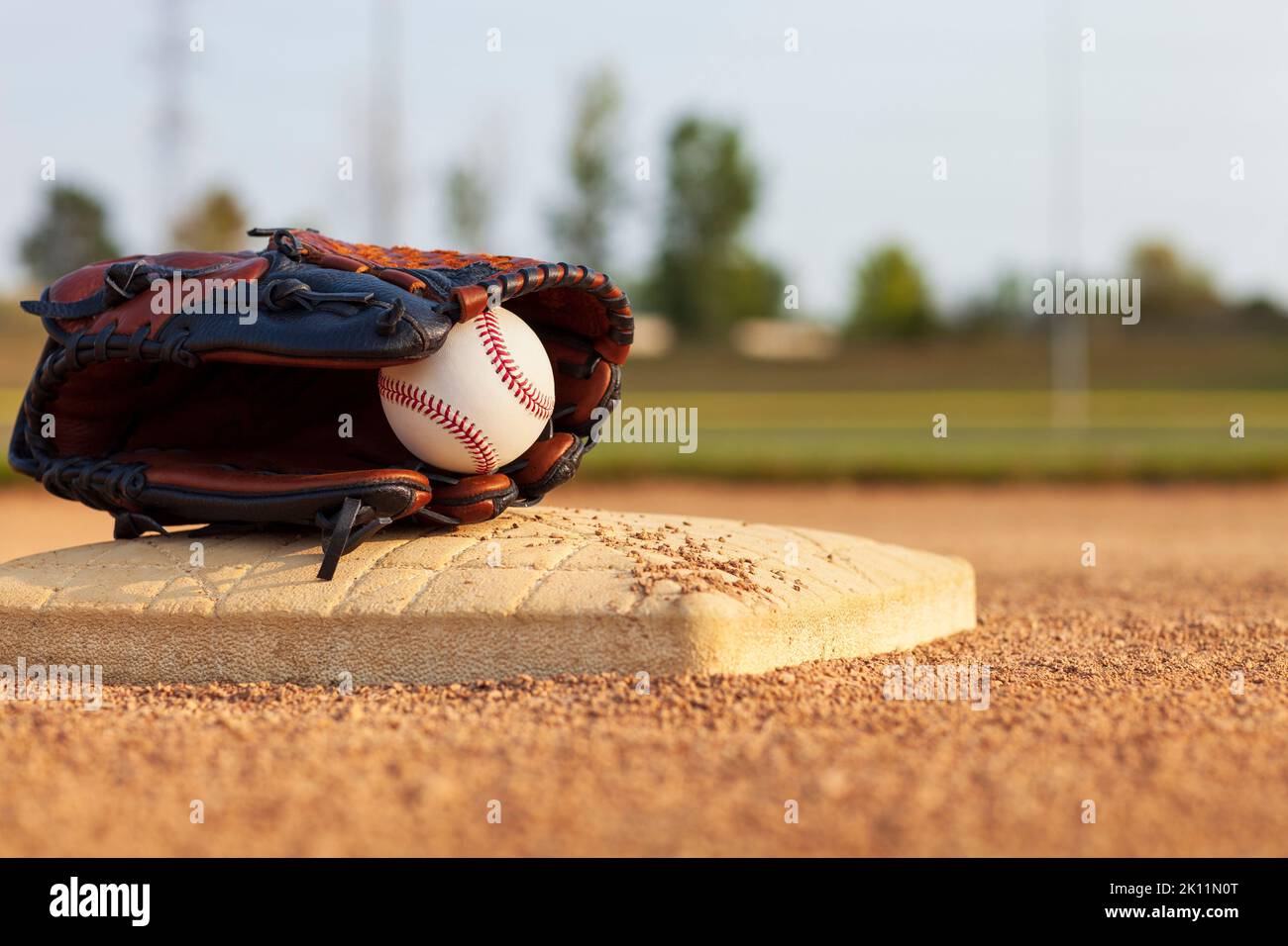 Selektiver Fokus eines Baseballs in einem Lederhandschuh auf einer Basis eines Baseballparks im Spielfeld an einem sonnigen Tag Stockfoto