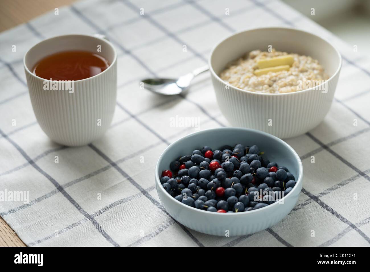 Gesundes Essen Frühstück mit Haferbrei Haferbrei in einer Schüssel mit Sommerbeeren, Butterscheibe, Tasse Tee. Stockfoto