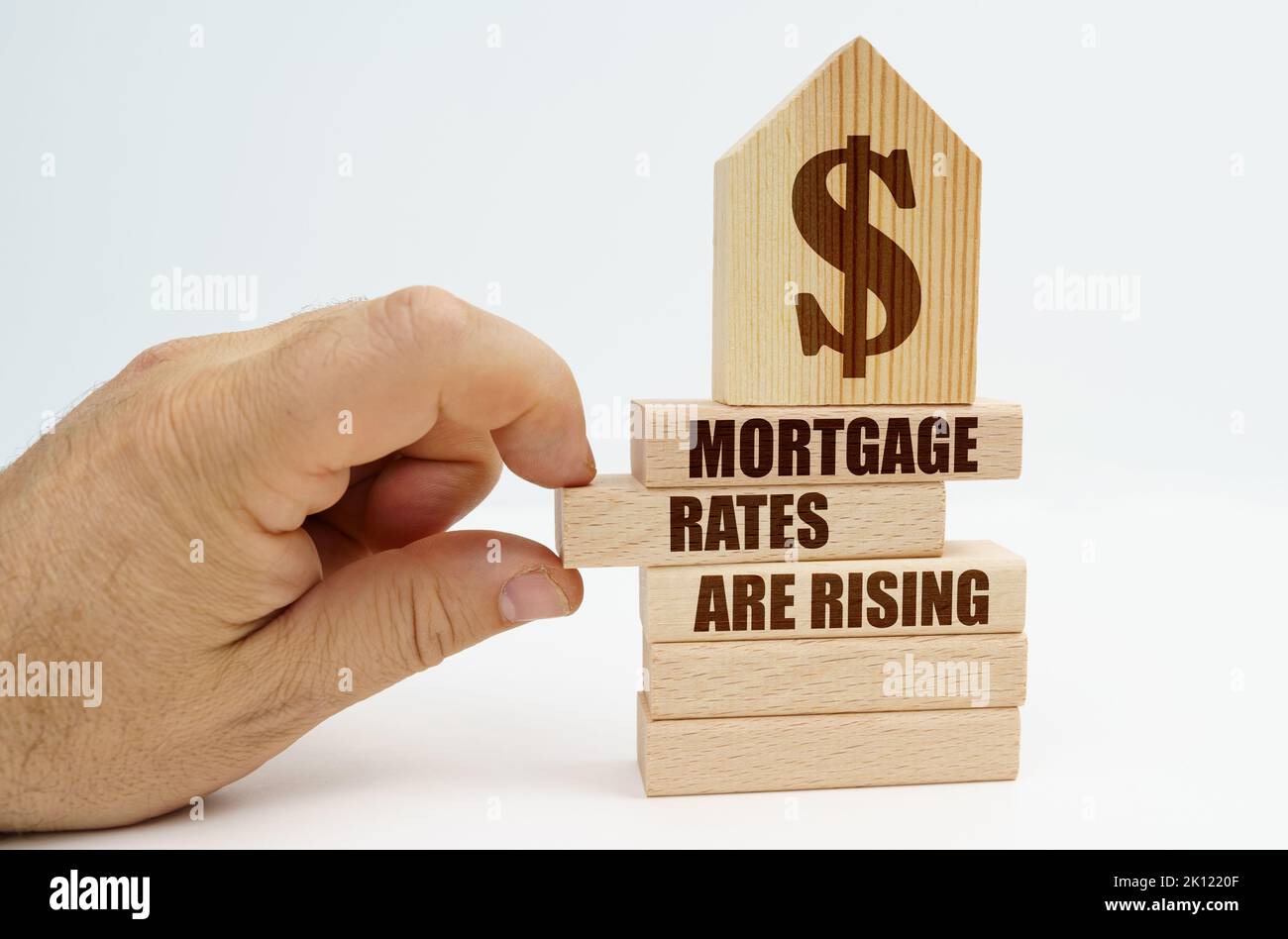 Immobilien und Geschäfte. Auf Holzblöcken mit der Aufschrift - die Hypothekenzinsen steigen, gibt es ein Modell eines Hauses mit einem Dollar-Symbol. Der Mann Stockfoto