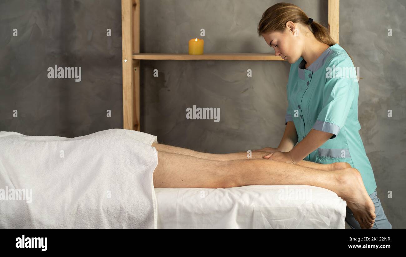 Weibliche Therapeutin, die Beinmassage an Sportler-Patienten auf dem Bett in der Klinik oder Spa. Sport-Physiotherapie Stockfoto