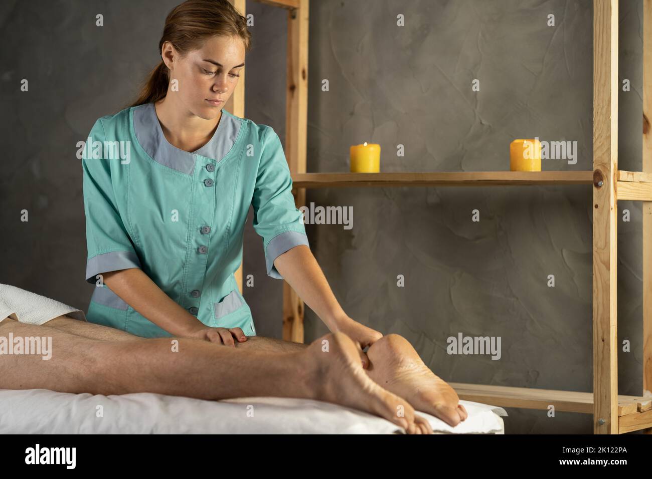 Junge Masseuse tun therapeutische Massage. Weibliche Masseurin arbeitet. Spa-Massage in einer gemütlichen häuslichen Umgebung. Bein-Massage-Therapie Stockfoto