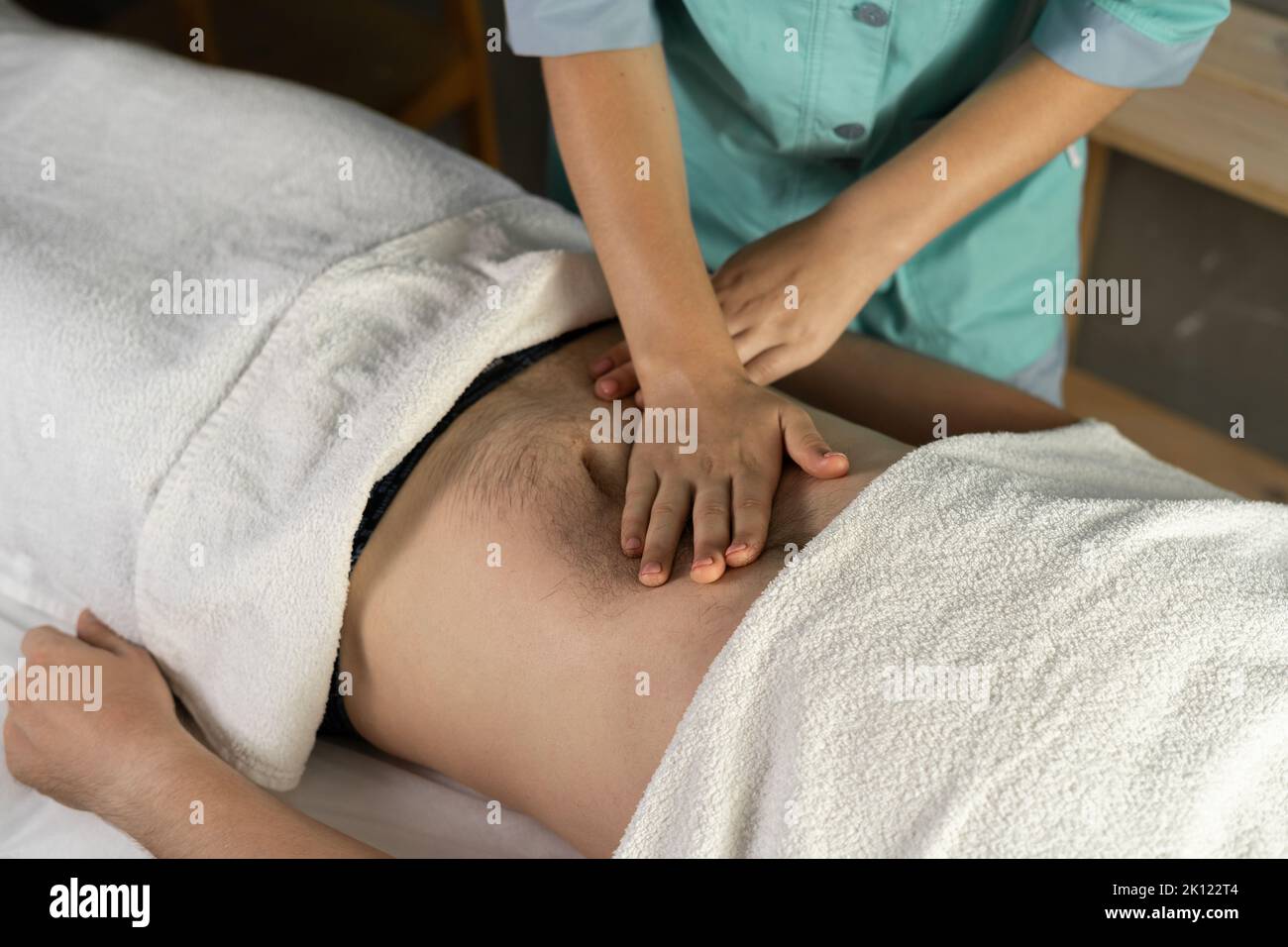 Weibliche Masseurin massiert einem jungen Mann in einem Spa-Raum die inneren Organe durch den Magen. Stockfoto