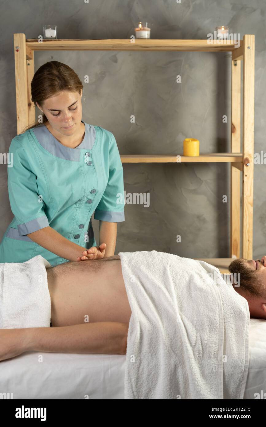 Weibliche Masseurin massiert einem jungen Mann in einem Spa-Raum die inneren Organe durch den Magen. Stockfoto