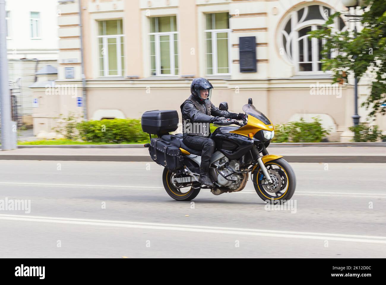 Motorradfahrer in schwarzer Lederuniform fährt schnell Motorrad durch die Stadt vorbei an Gebäuden über der Stadtstraße Tomsk Russland 10. August 2022, selektiver Fokus Stockfoto