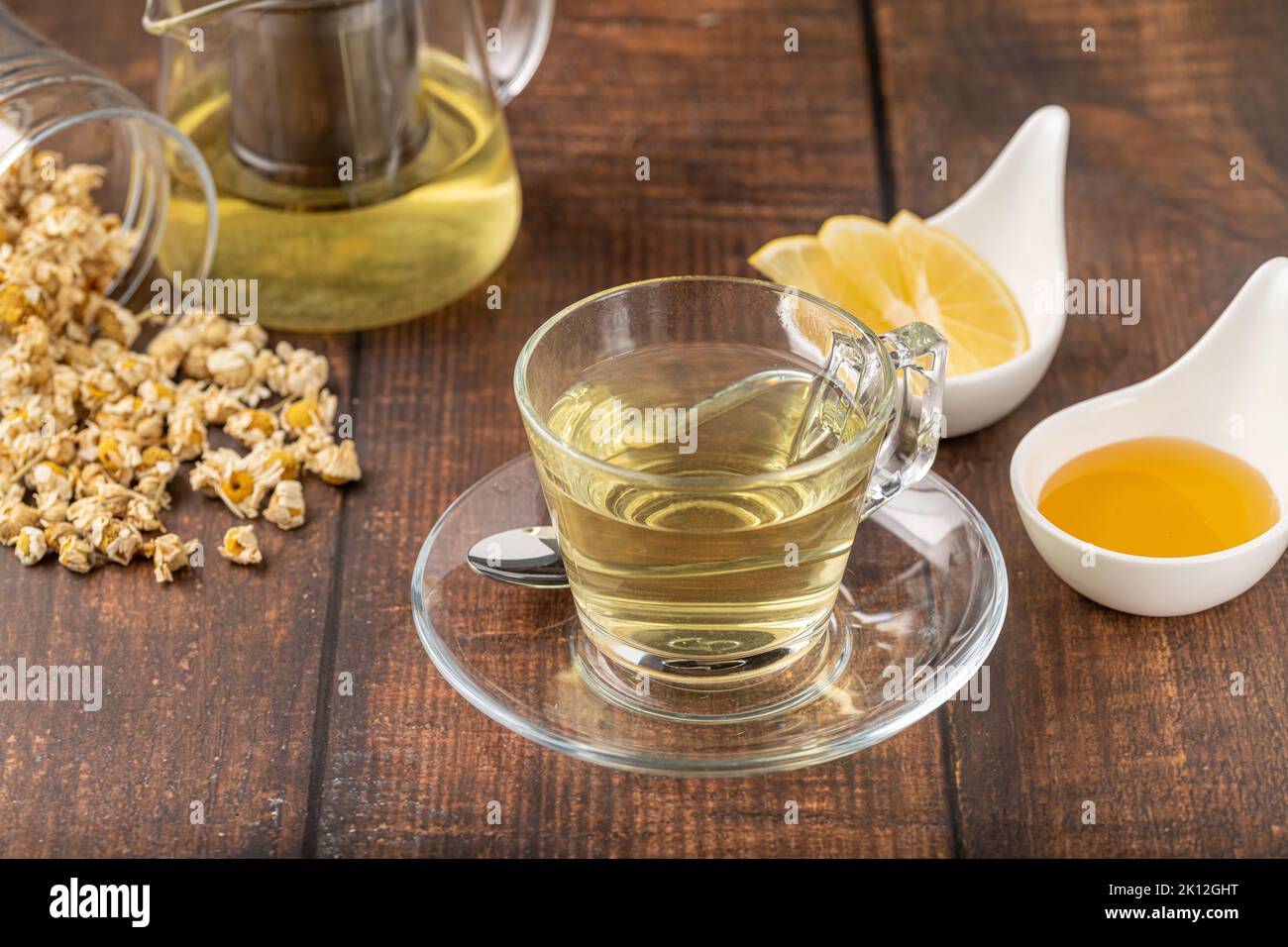 Entspannender Kamillentee in einer Glasschale mit Zitronenscheiben und Honig daneben auf einem Holztisch. Stockfoto