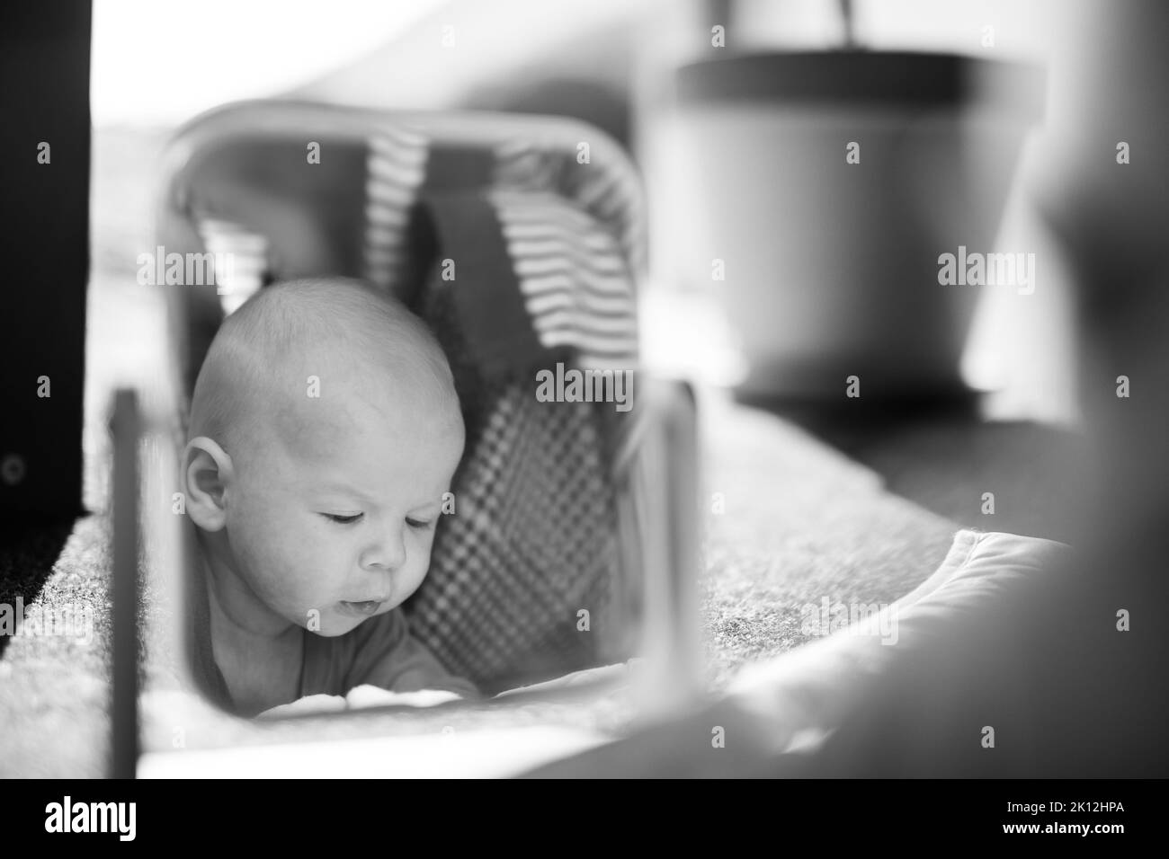 Schöne Aufnahme eines niedlichen Jungen, der seine Spiegelung im Spiegel betrachtet. Schwarzweiß-Bild. Stockfoto