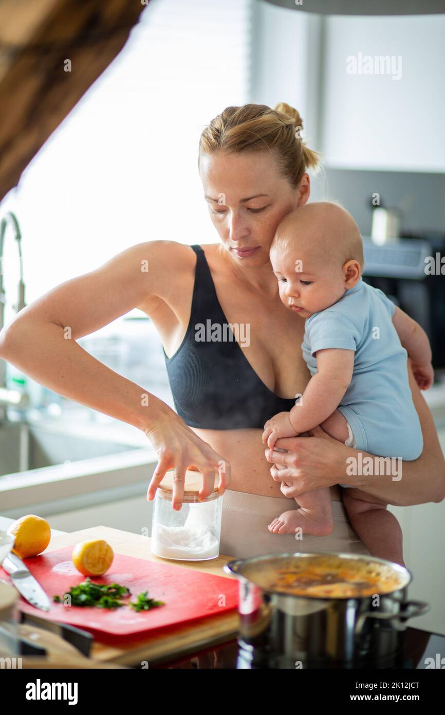 Frau kocht, während sie ihren vier Monate alten Jungen in den Händen hält Stockfoto