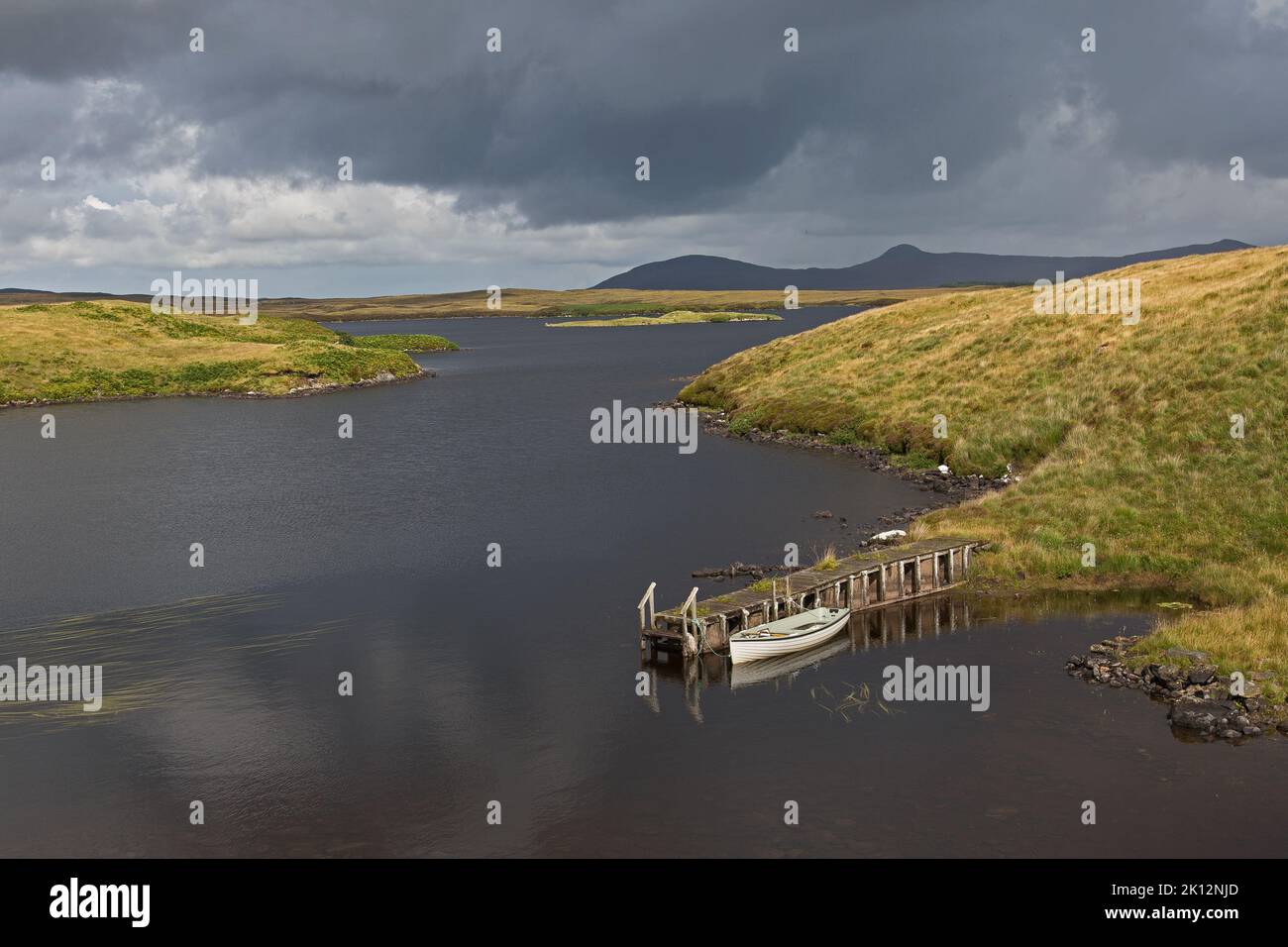 Schwere Wolken über sonnigem Loch und Bootsanleger in Magic Light, Uist, North Uist, Hebriden, Äußere Hebriden, Western Isles, Schottland, Vereinigtes Königreich Stockfoto