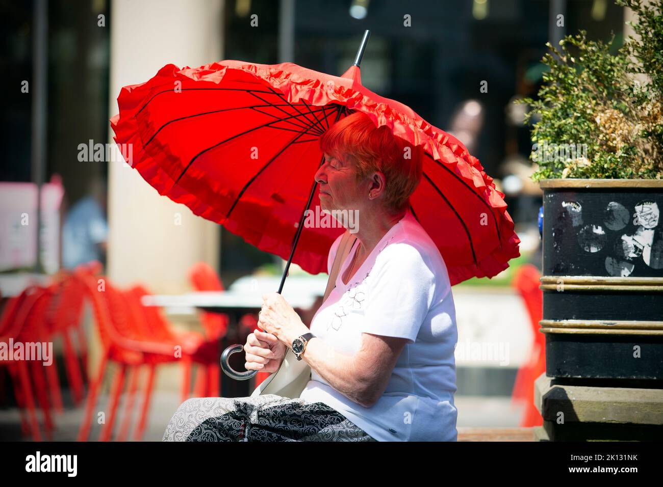 Eine Frau mit einem großen roten Regenschirm nimmt Schutz vor der Sonne, während die Menschen in der Stadt York, North Yorkshire, den heißesten Tag der Aufzeichnung als die te aushalten Stockfoto