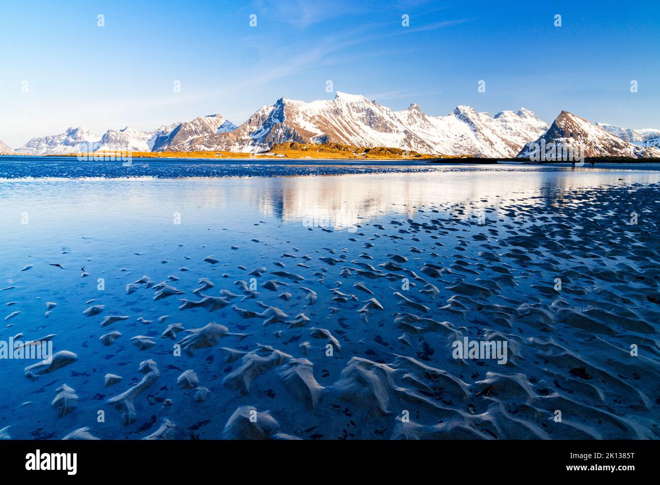Wellen des kalten Meeres krachen am Strand mit schneebedeckten Bergen im Hintergrund, Fredvang, Nordland, Lofoten Islands, Norwegen, Europa Stockfoto