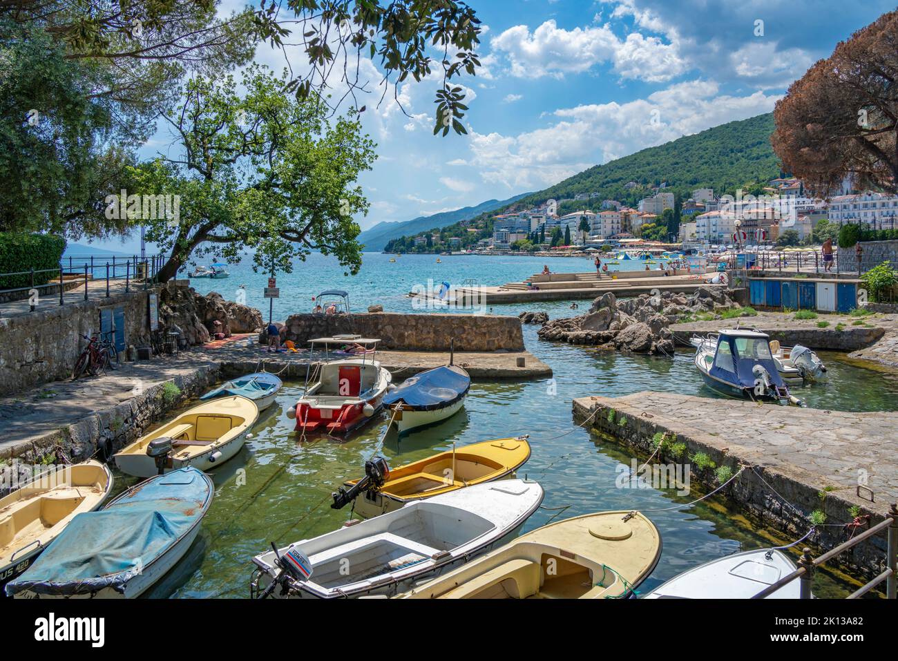 Blick auf felsigen Einlass und Boote mit Stadt Opatija im Hintergrund, Opatija, Kvarner Bucht, Kroatien, Europa Stockfoto