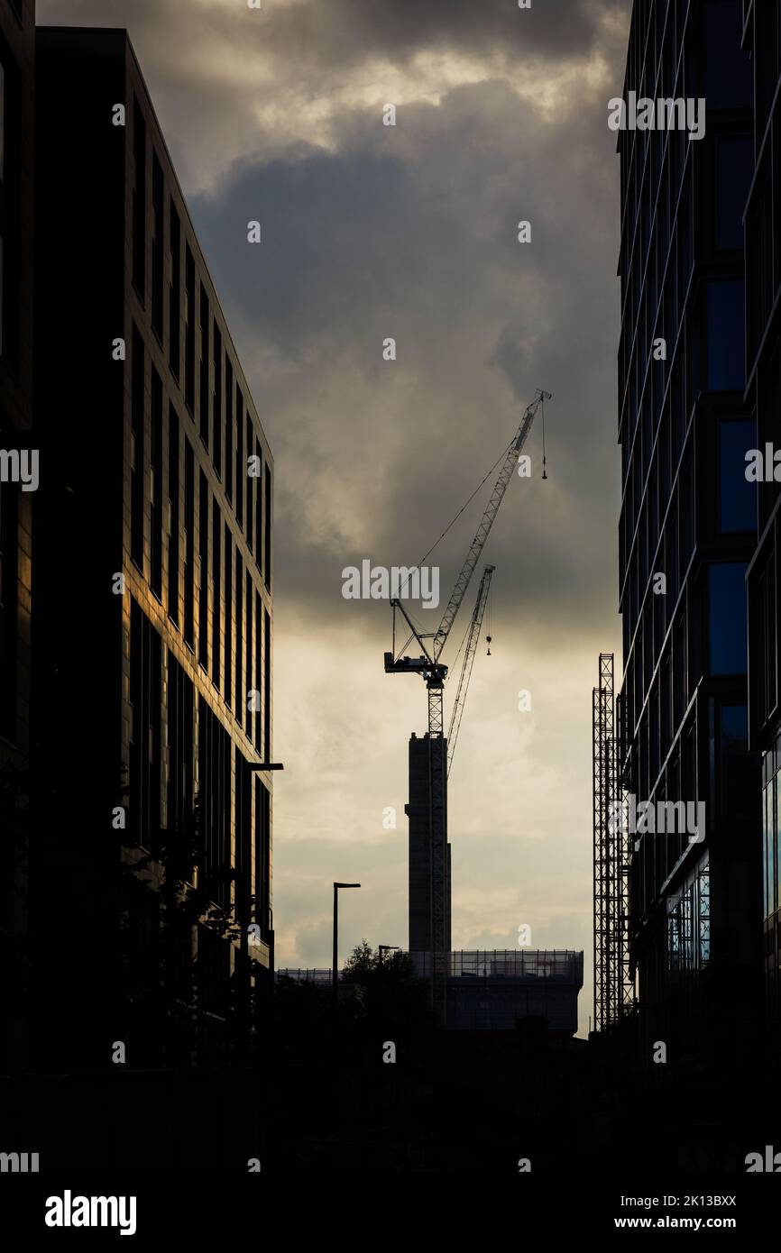 Ein hoher Baukran, der hohe Wolkenkratzer in einer Stadt errichtet, in einem Bild von Erneuerung und Investitionen der Industrie Stockfoto