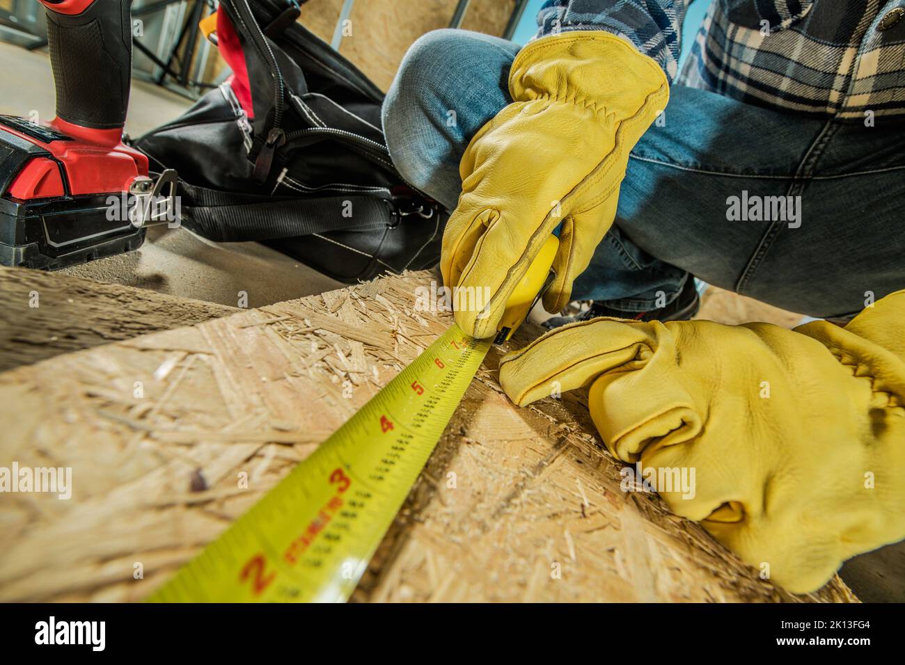 Nahaufnahme Foto des Bauarbeiters in gelben Schutzhandschuhen Messen des Oriented Strand Boards mit Tapeline, bevor ein Schnitt gemacht wird. Stockfoto