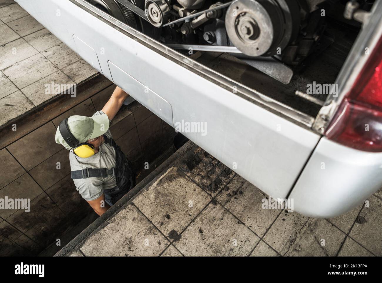 Kaukasischer Mechaniker, der in der Inspektionsstelle an der Fahrzeugkontrollstation steht und die regelmäßige technische Prüfung des Fernmotorwagens durchführt. Engi Stockfoto