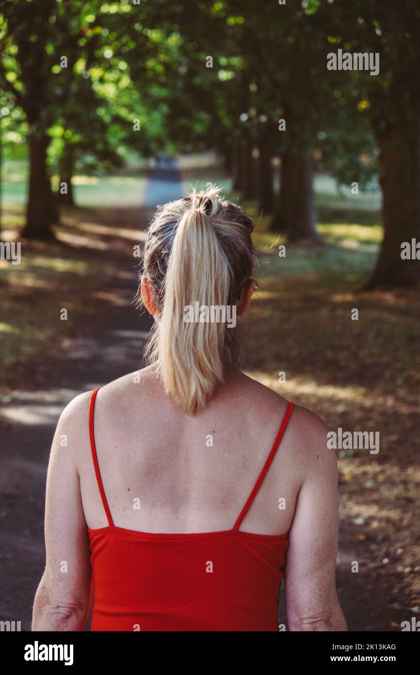 Rückansicht einer Frau, die mit einem roten Oberteil durch eine Packung läuft Stockfoto