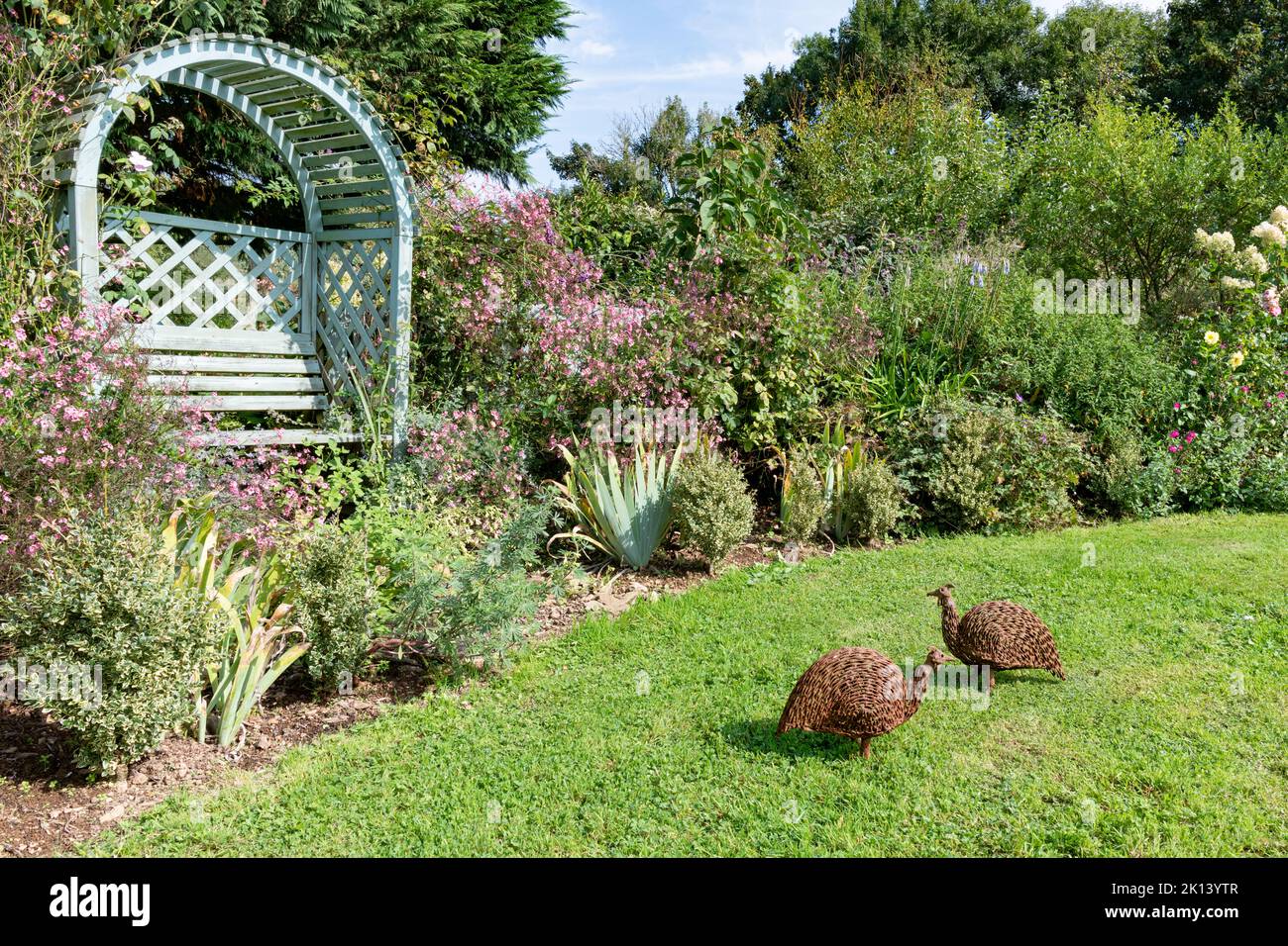 Hübscher bogenförmiger Gartensitz in einem englischen Landgarten mit zwei Vogelskulpturen Stockfoto