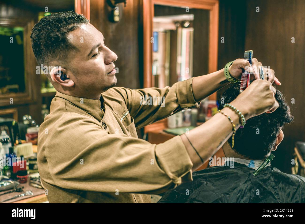 Junger behinderter Barbier mit Hörgerät, der in einem Friseurladen Haare eines Mannes schneidet. Stockfoto
