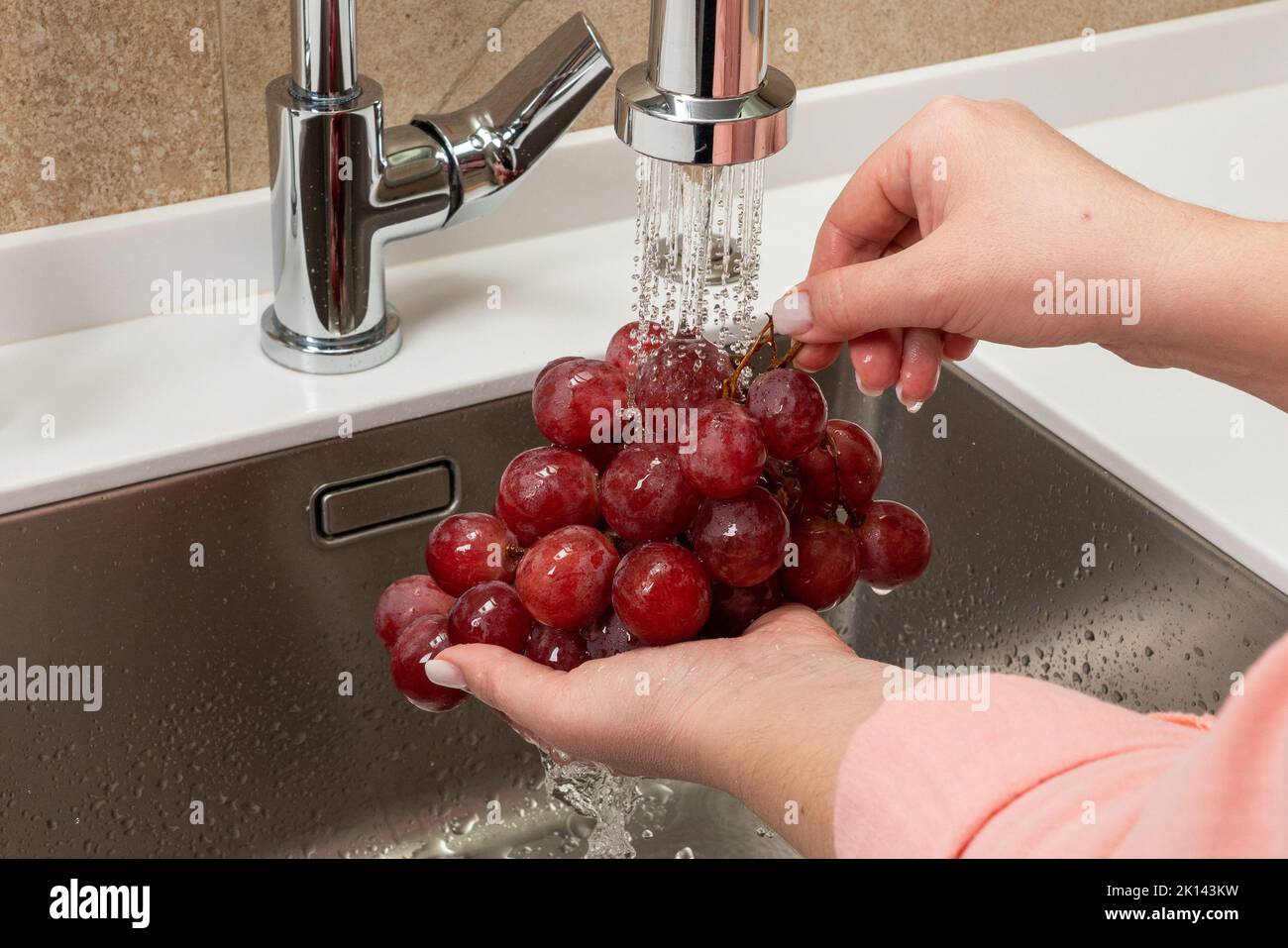 Mädchen wäscht rote Trauben in der Küche Stockfoto