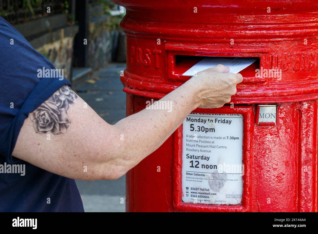 Eine Person, die einen Brief in einer traditionellen roten Säulenbox, London, Großbritannien, postet Stockfoto