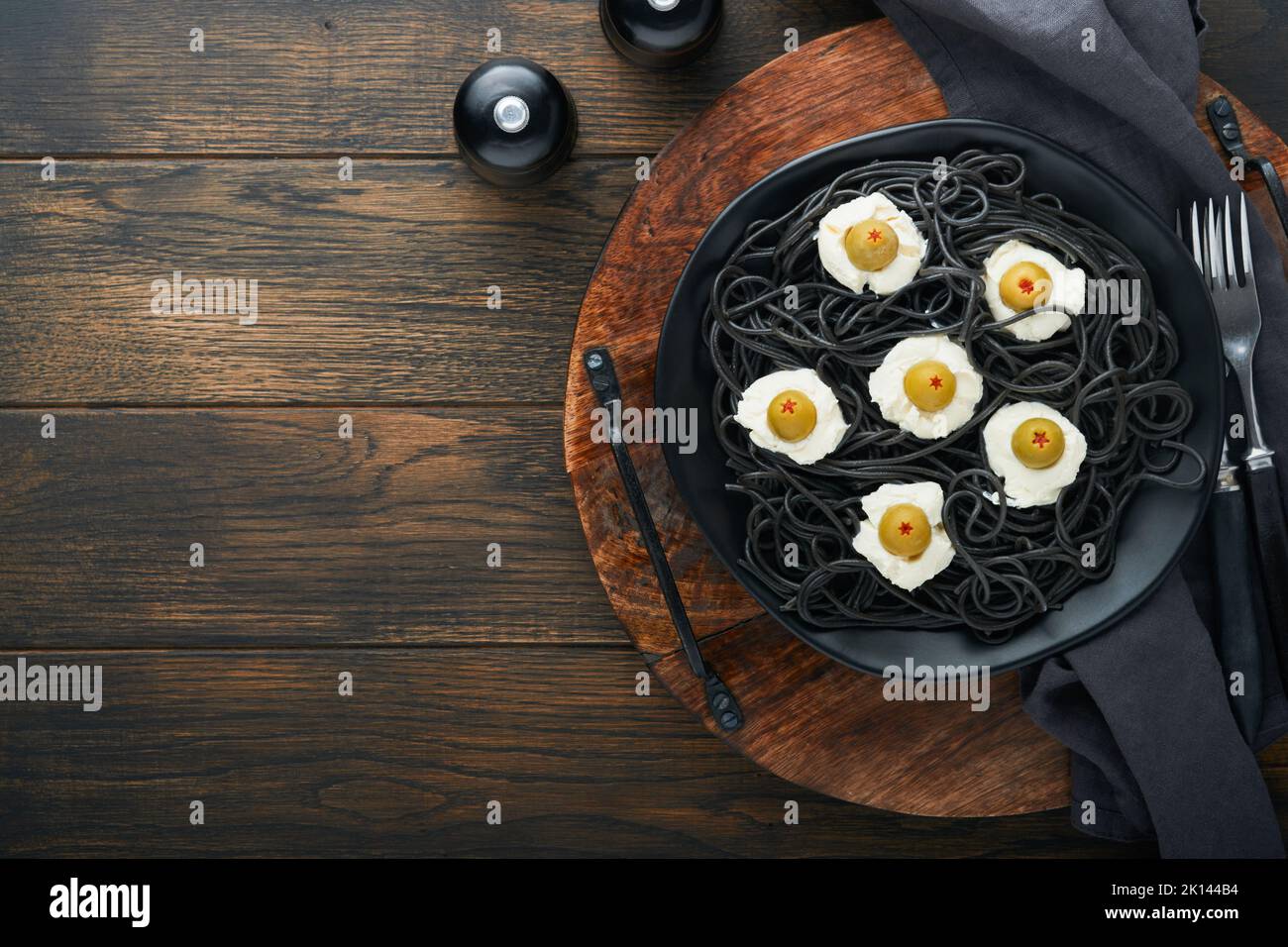 Halloween Party italienische schwarze Pasta dekoriert Horror Oliven wie Augen auf schwarzem Teller auf alten dunklen Tisch Hintergrund. Monster Gesicht von Pasta. Halloween Stockfoto