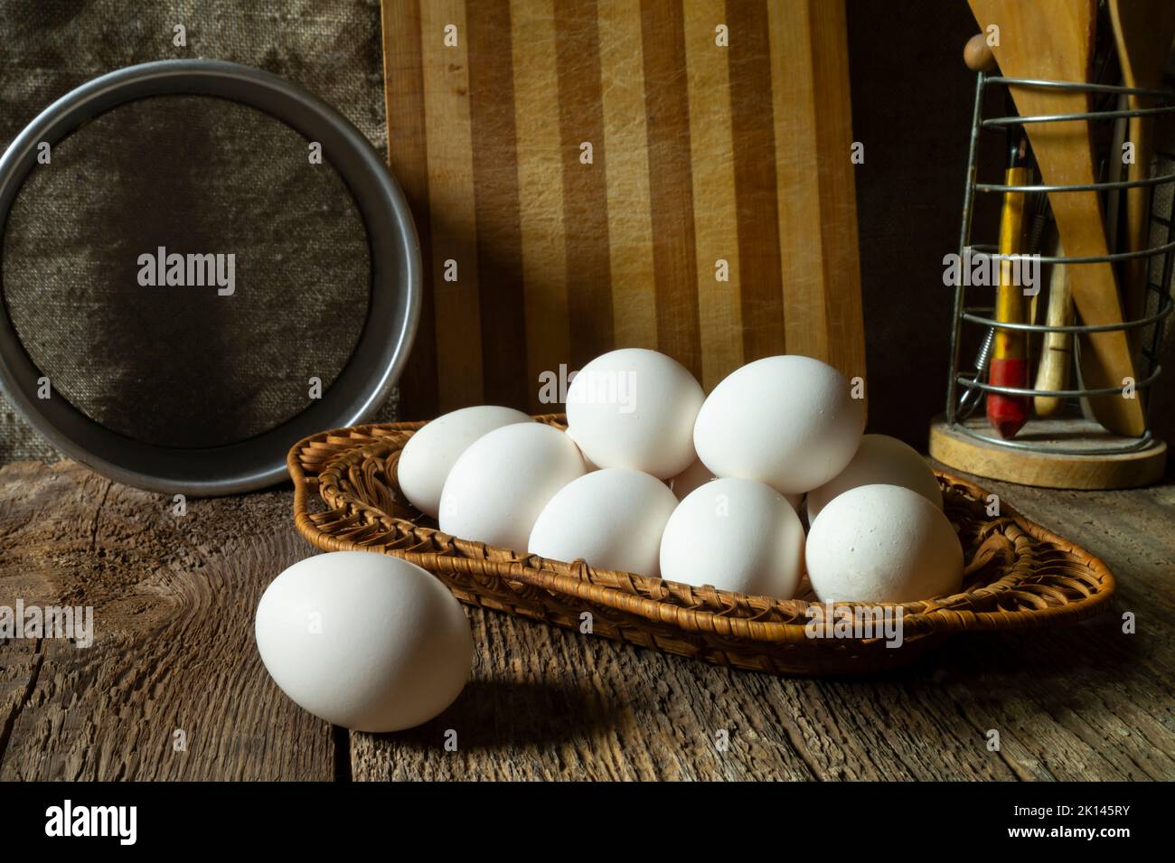 Stillleben mit Hühnereiern und Küchenutensilien. Die Gegenstände liegen auf einem alten Holztisch Stockfoto