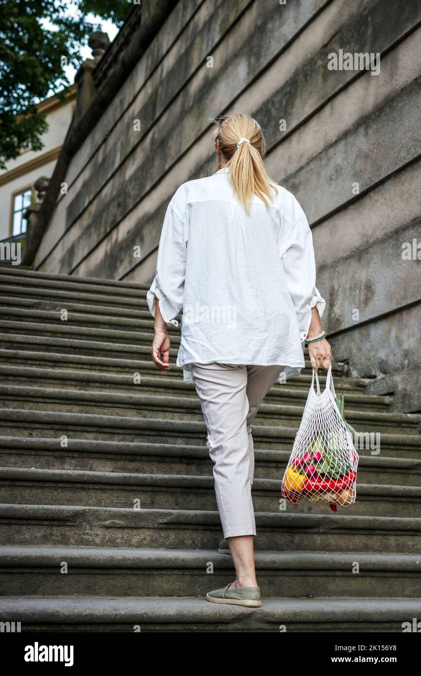 Frau, die an Treppen läuft und wiederverwendbare Netztaschen in der Altstadt trägt Stockfoto