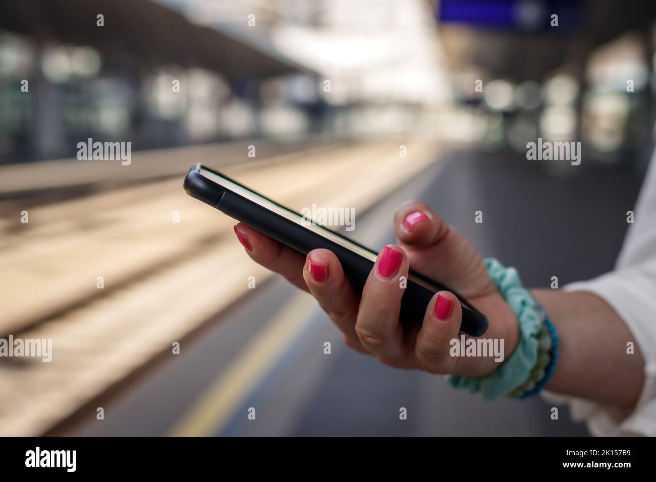 Frau überprüft Zugverspätung auf Smartphone-Handy-App am Bahnhof Stockfoto